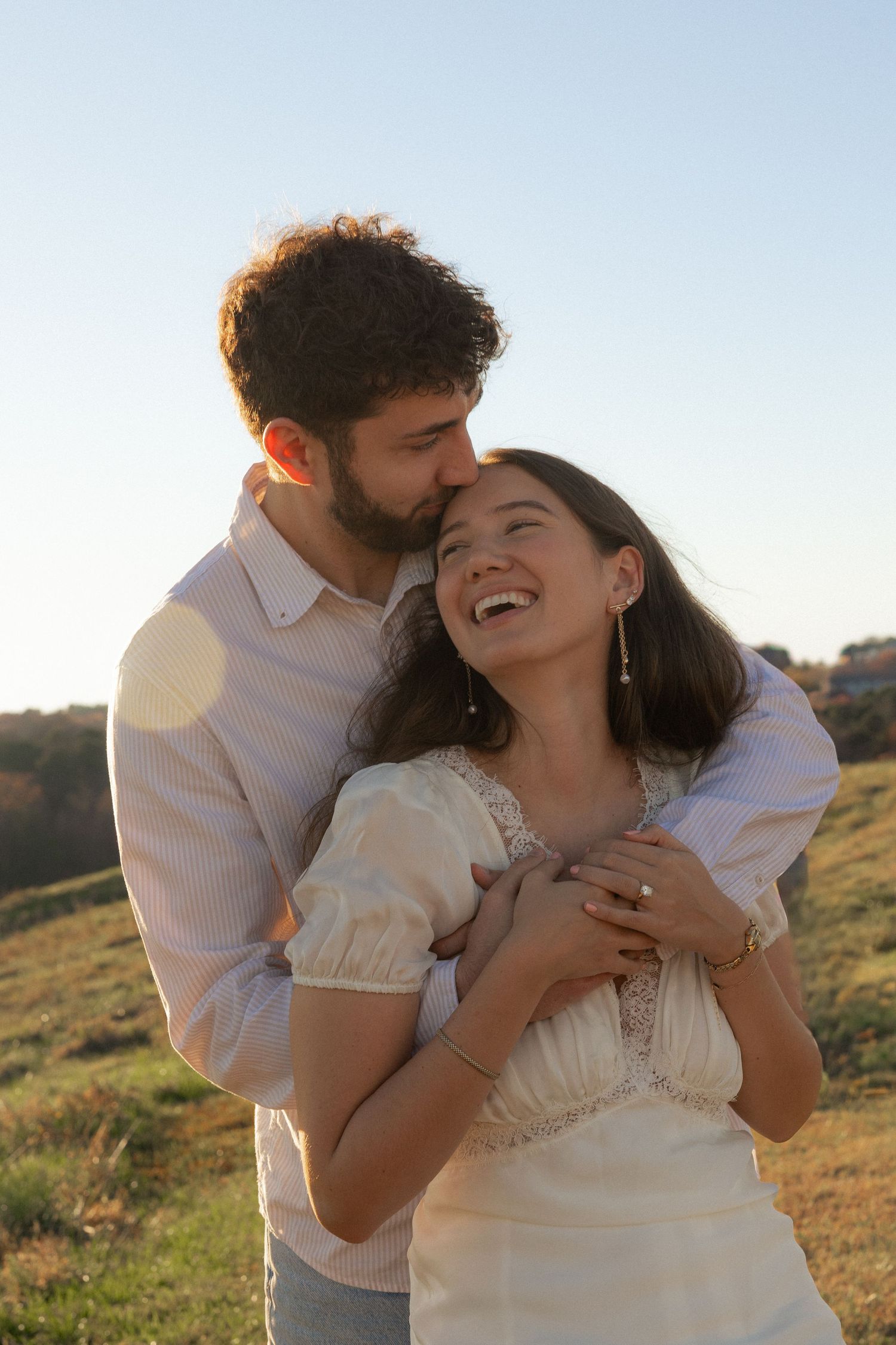 A couple embraces lovingly in a sunny field during golden hour as they share tender romantic moments together.