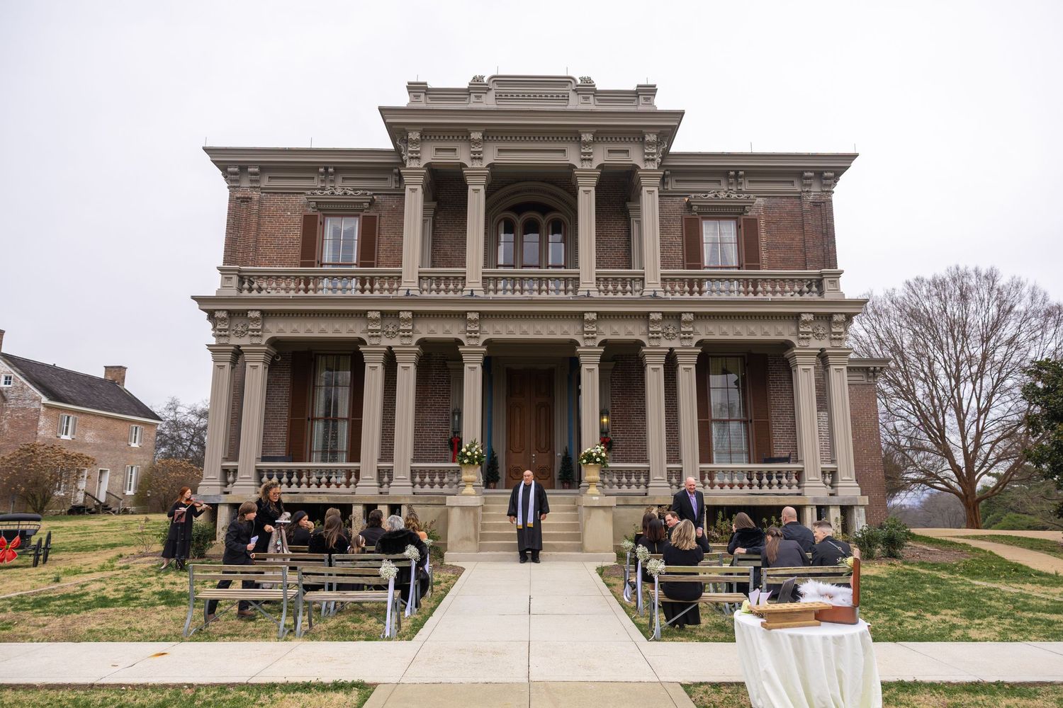 A historic Victorian-style mansion with grand columns serves as an elegant wedding venue with guests gathered outside.