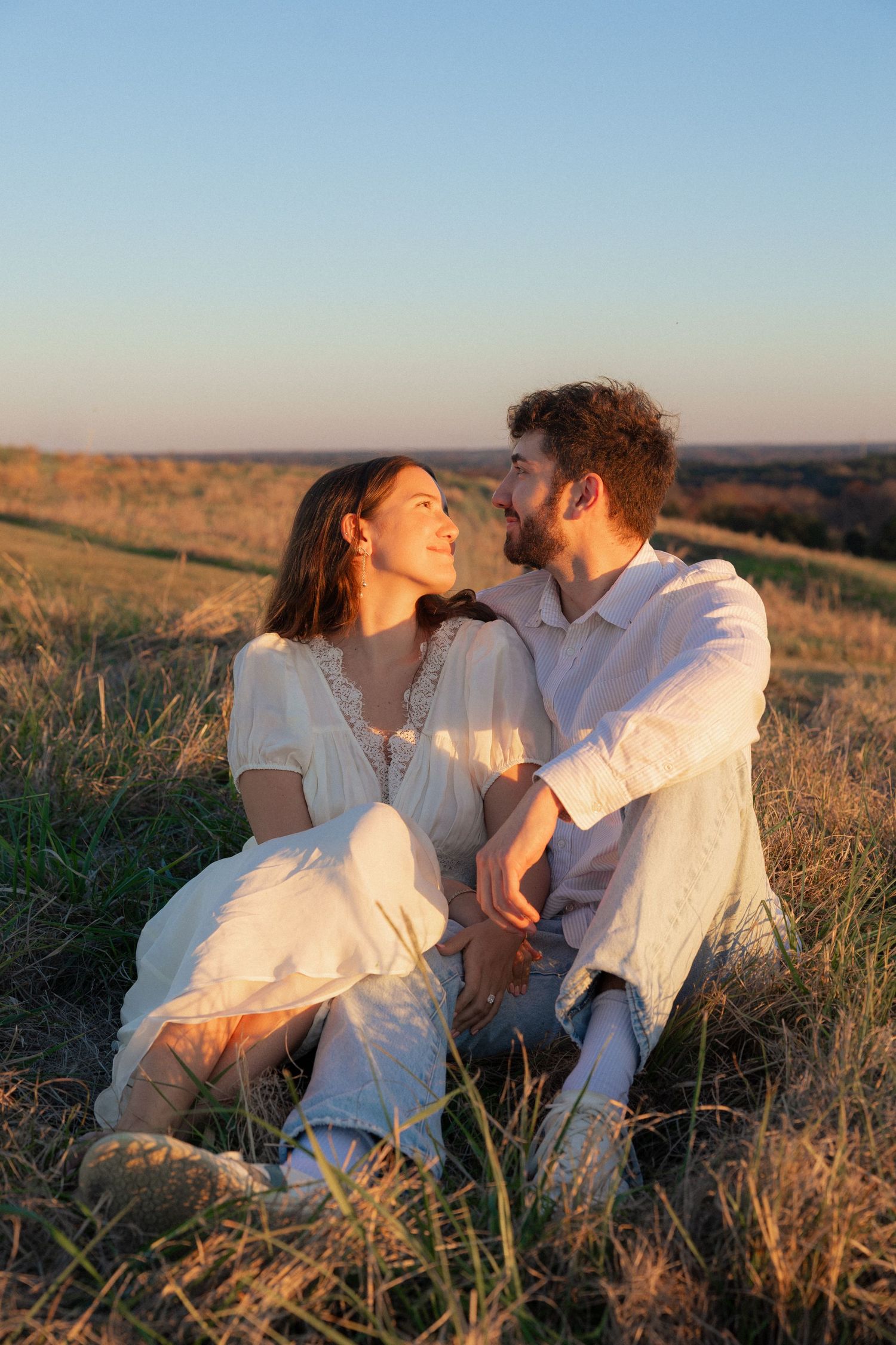 Couple dressed in white shares intimate moments while relaxing in a sunlit meadow.