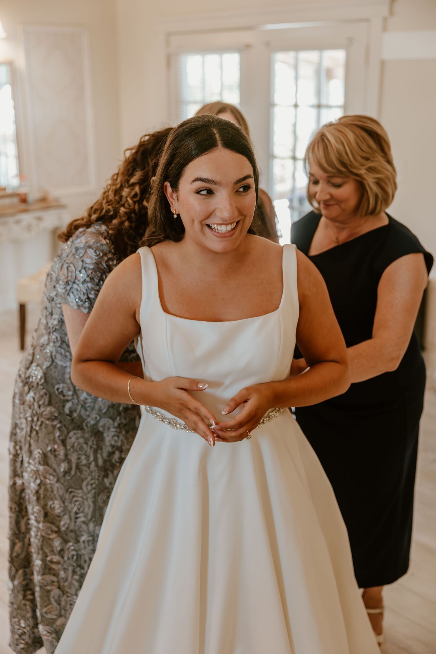 Bride trying on elegant white wedding dress in bright indoor setting.