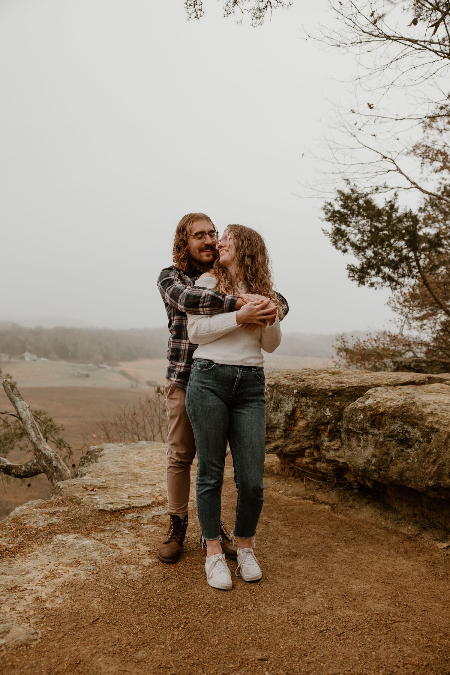 Tender moment shared between couple on natural stone platform with rolling hills in background.