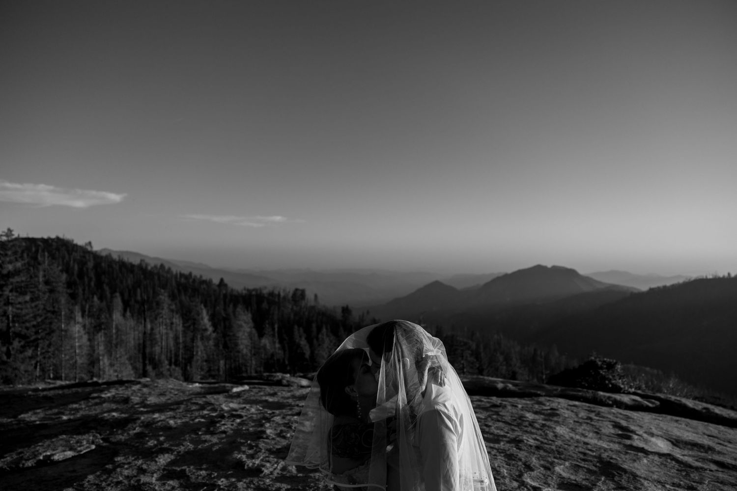Black and white panoramic view of mountainous landscape with couple silhouetted against sky.
