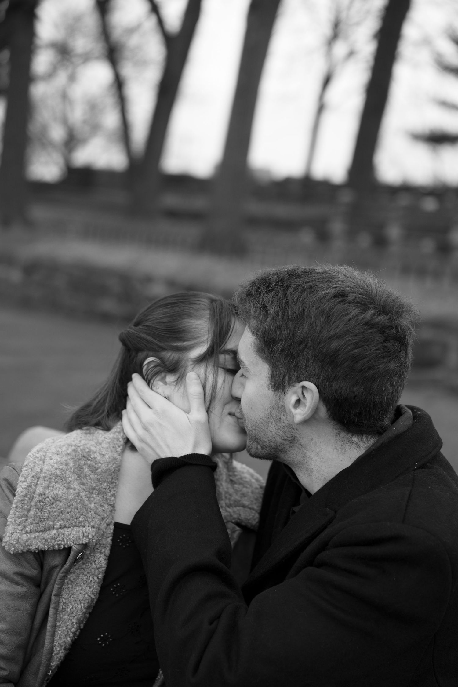 A romantic couple sharing an intimate kiss outdoors in black and white photography.