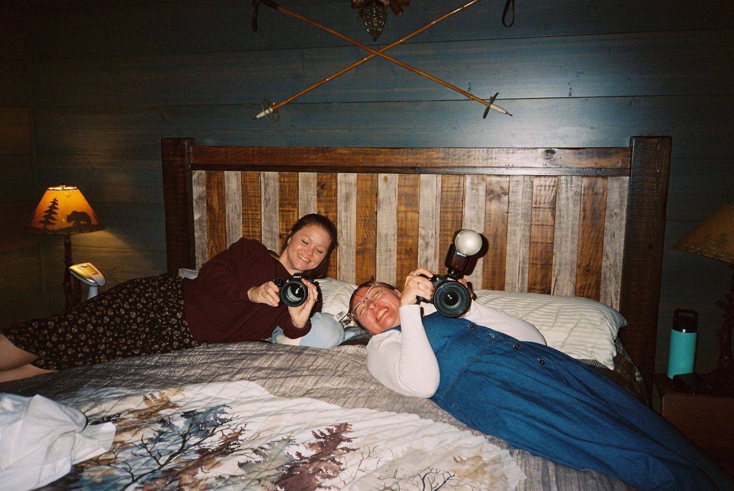 People relaxing on a rustic wooden bed with cozy blankets in a dimly lit room with wall sconces.