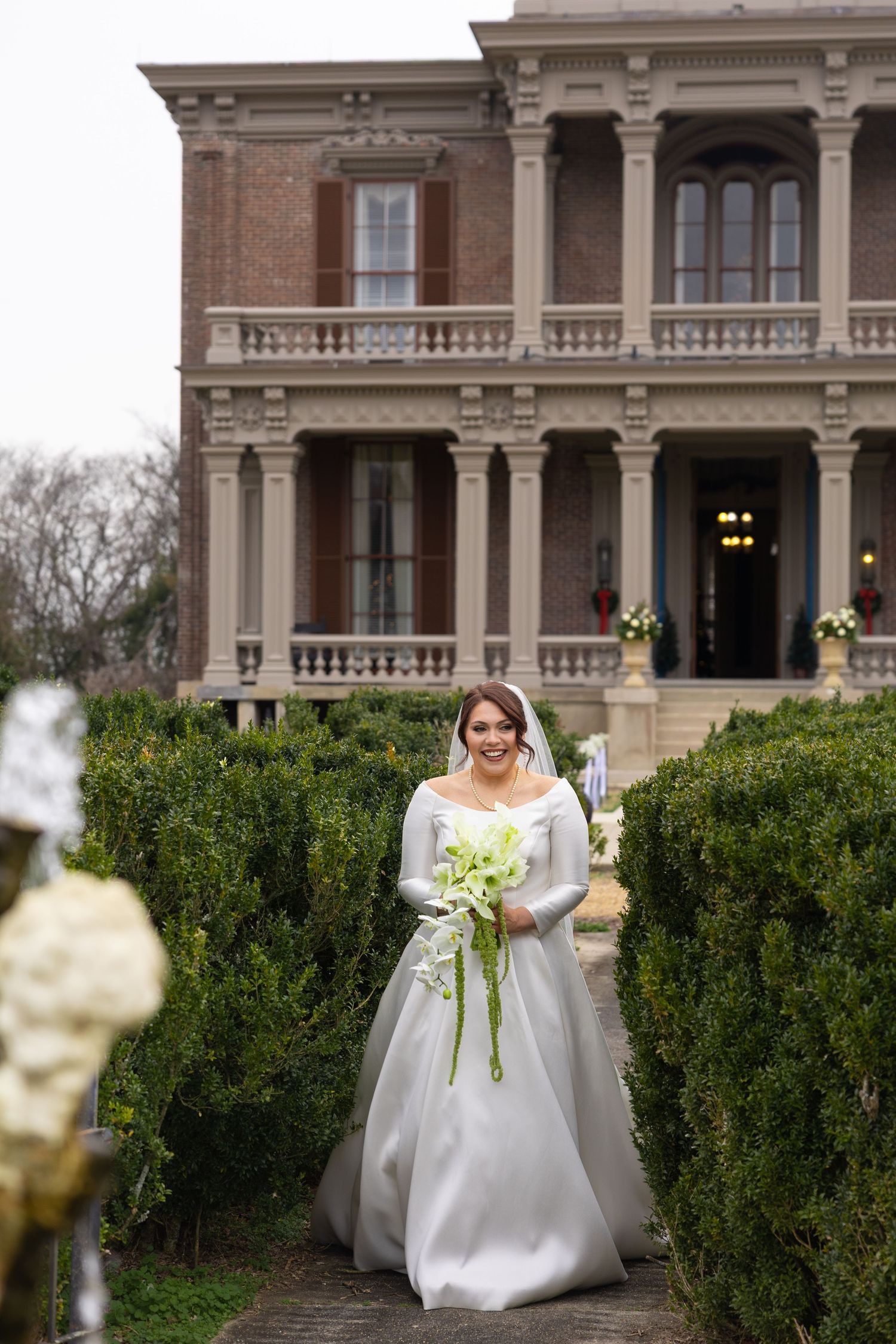 Formal garden pathway with manicured hedges and classical architecture of a historic mansion in the background.