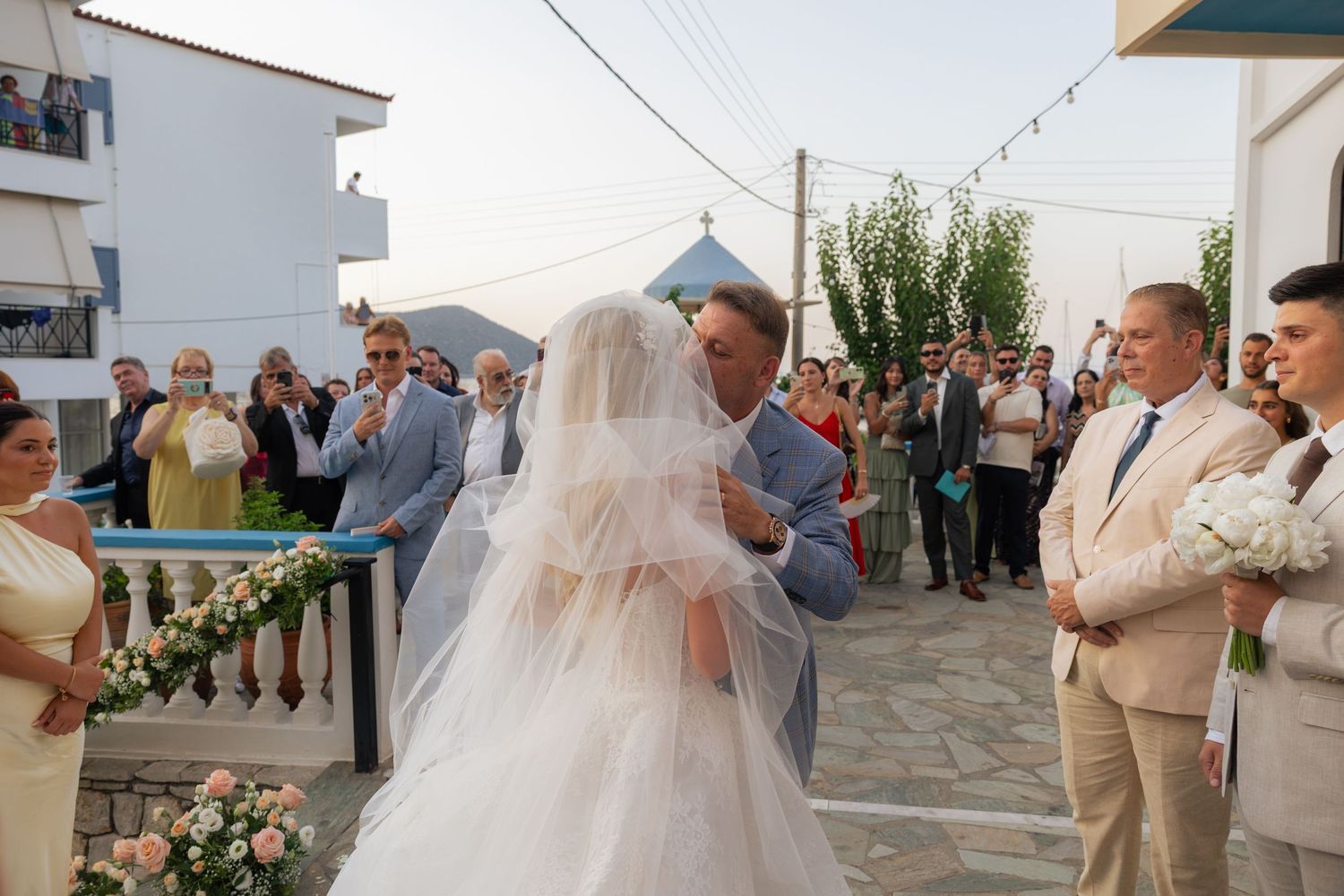 A wedding party gathers outside a white Mediterranean-style building during a celebration.
