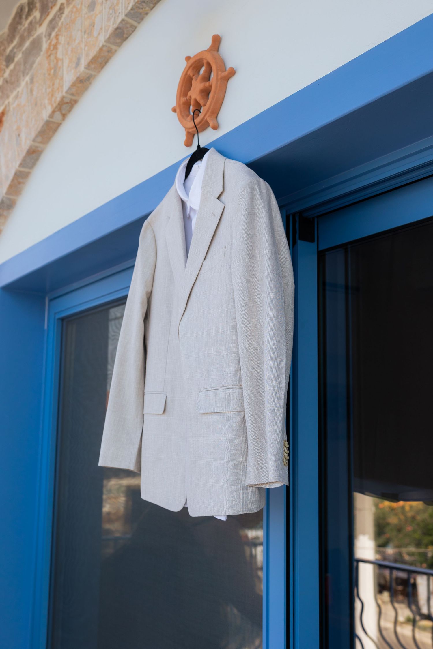 A light gray suit jacket hangs against a blue wall in natural sunlight.