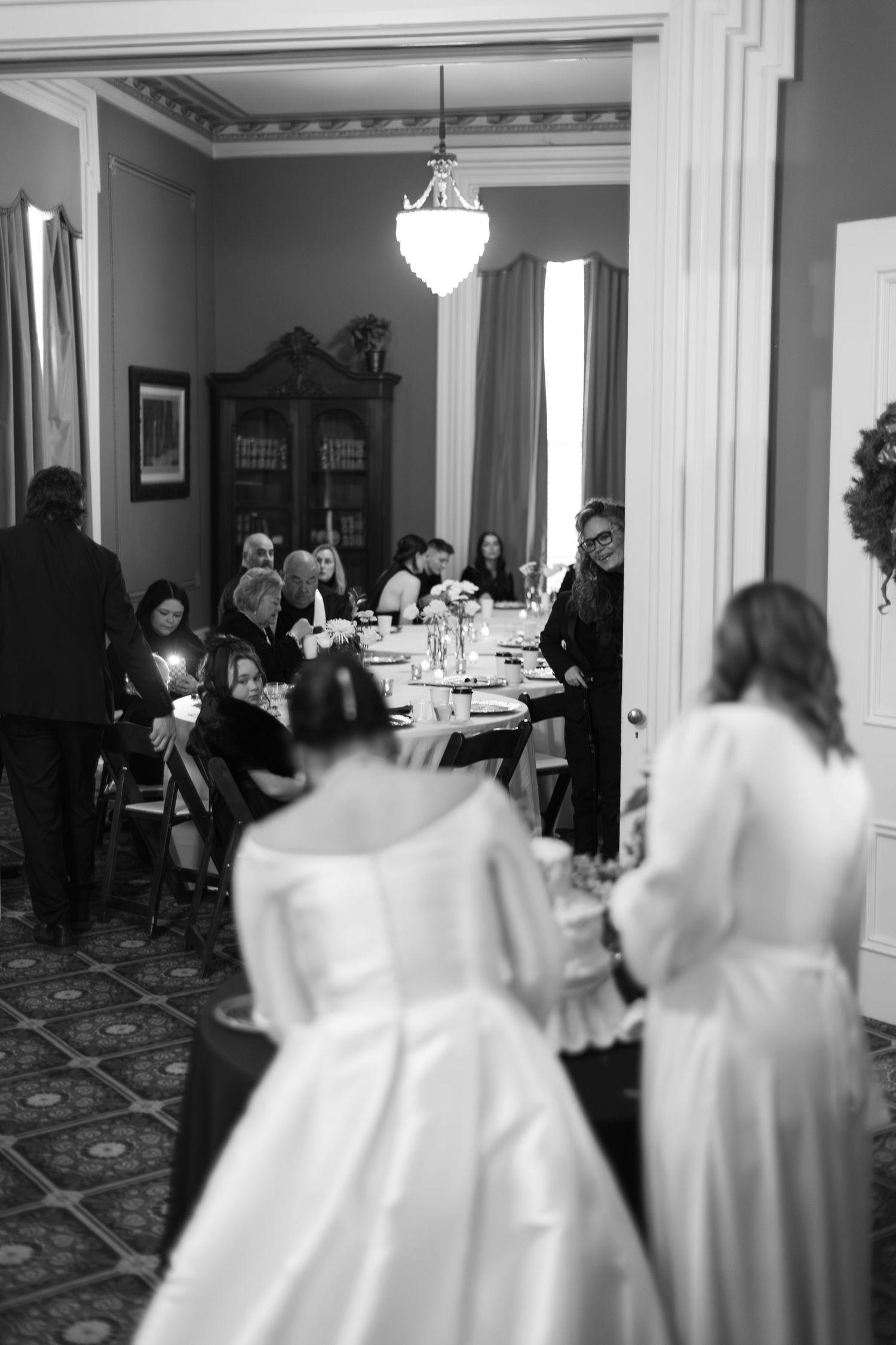 Wedding reception scene in an elegant white room with formal table settings and guests in formal attire.