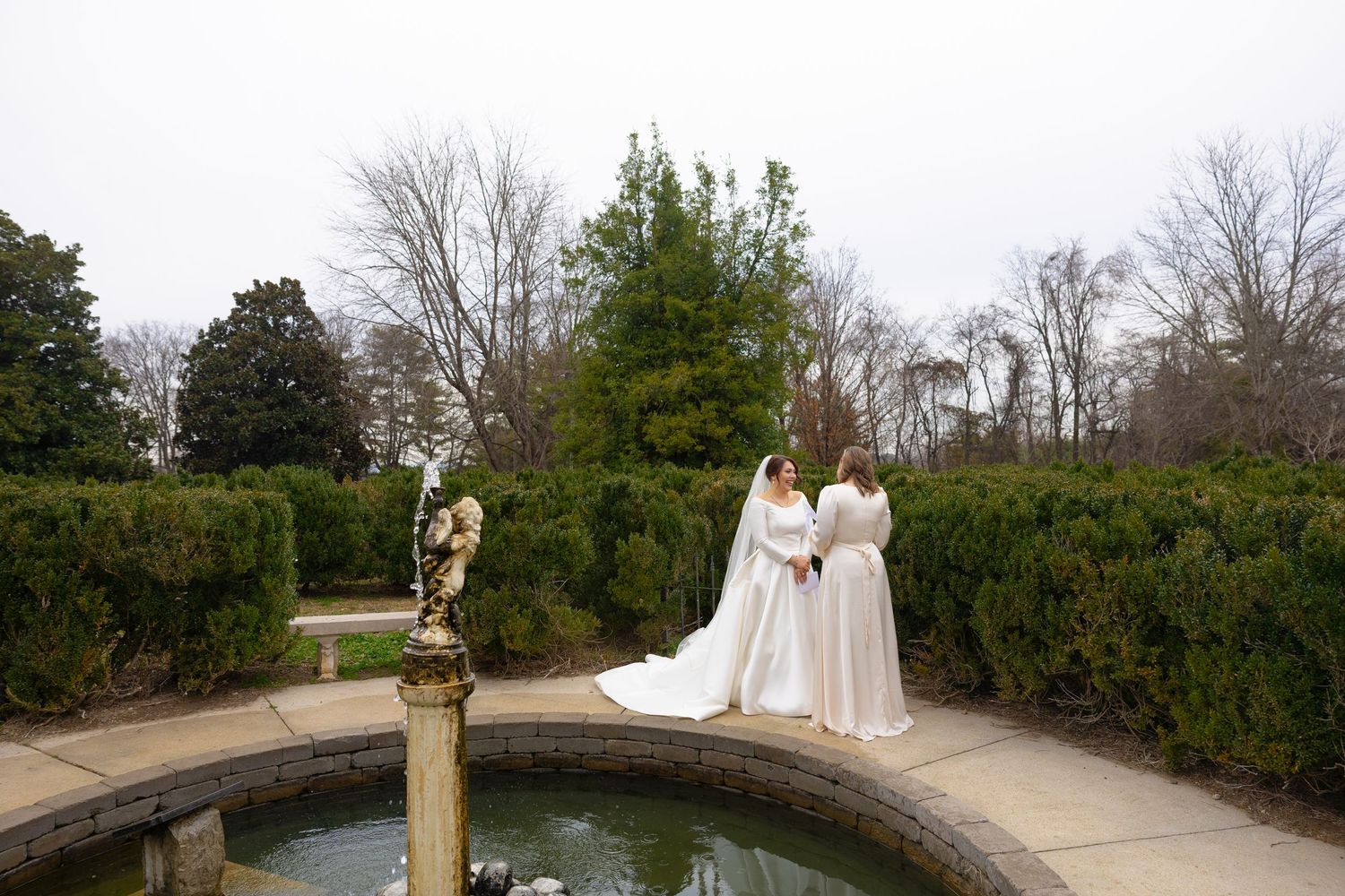 A romantic winter wedding photoshoot at a historic garden venue with snow-covered pathways and evergreen landscaping.