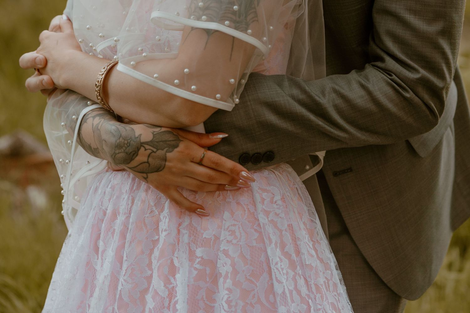 Close-up detail of embrace between bride in lace dress and groom in grey suit.