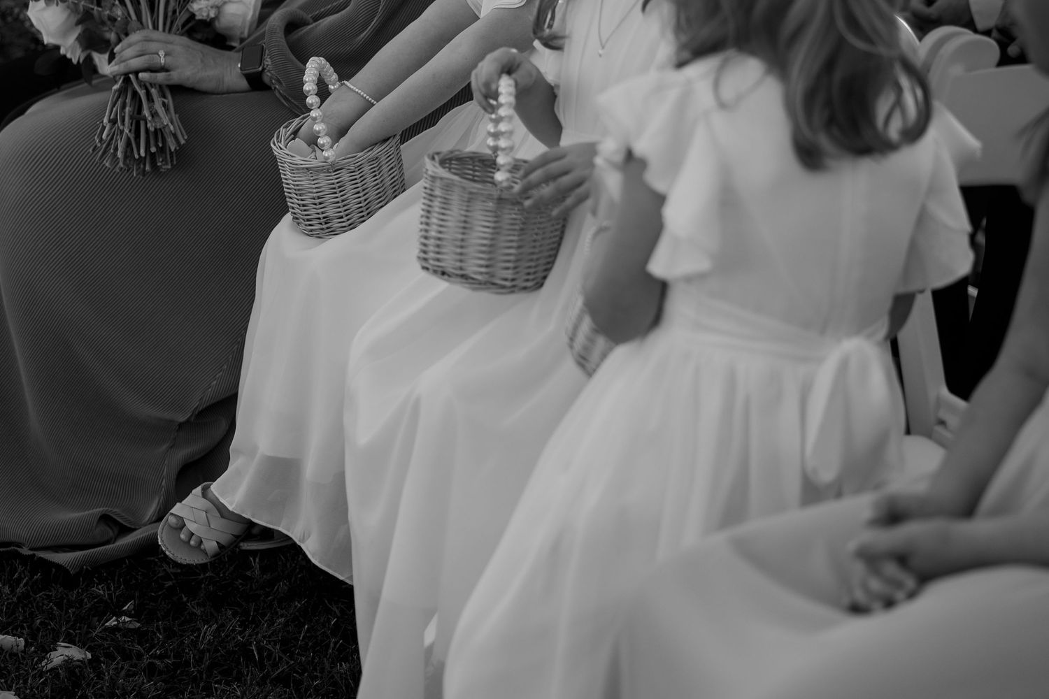 Black and white image of flower girls in white dresses holding wicker baskets.