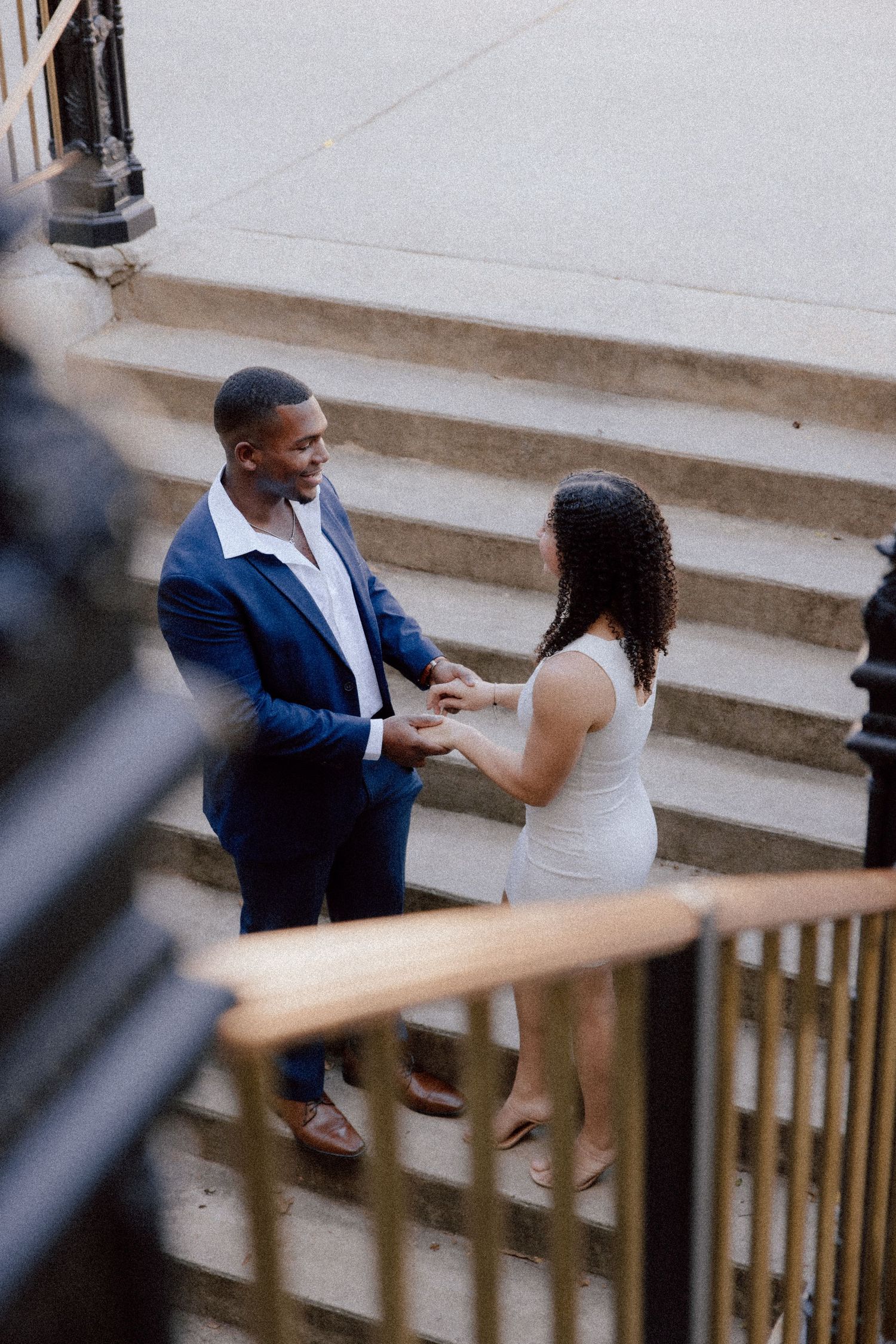 A couple stands on stone steps during what appears to be a surprise proposal moment.