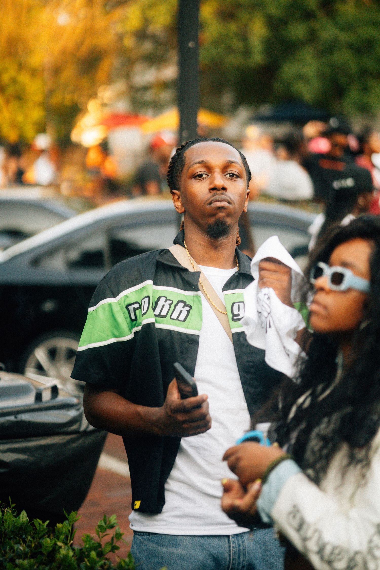 Person wearing a black and white jacket with green stripe stands outdoors on an autumn day with blurred background.USC Hip Hop Wednesday