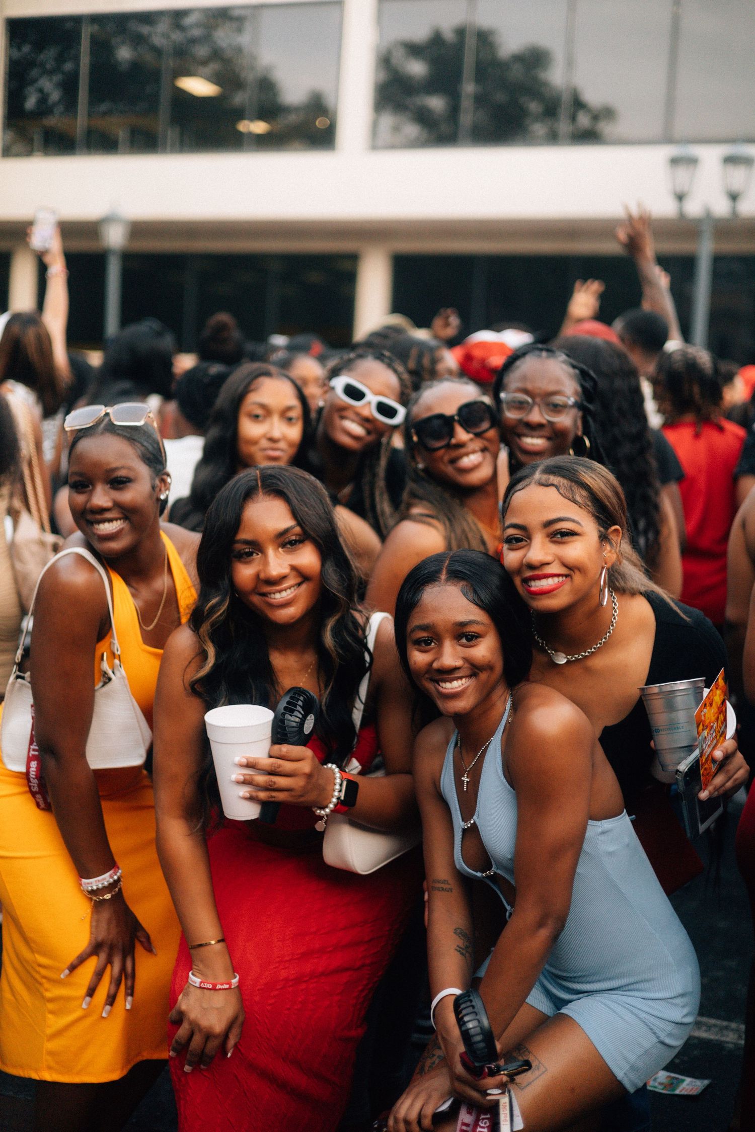 A group of friends in colorful outfits smile together at an outdoor social gathering while holding drinks. USC Hip Hop Wednesday