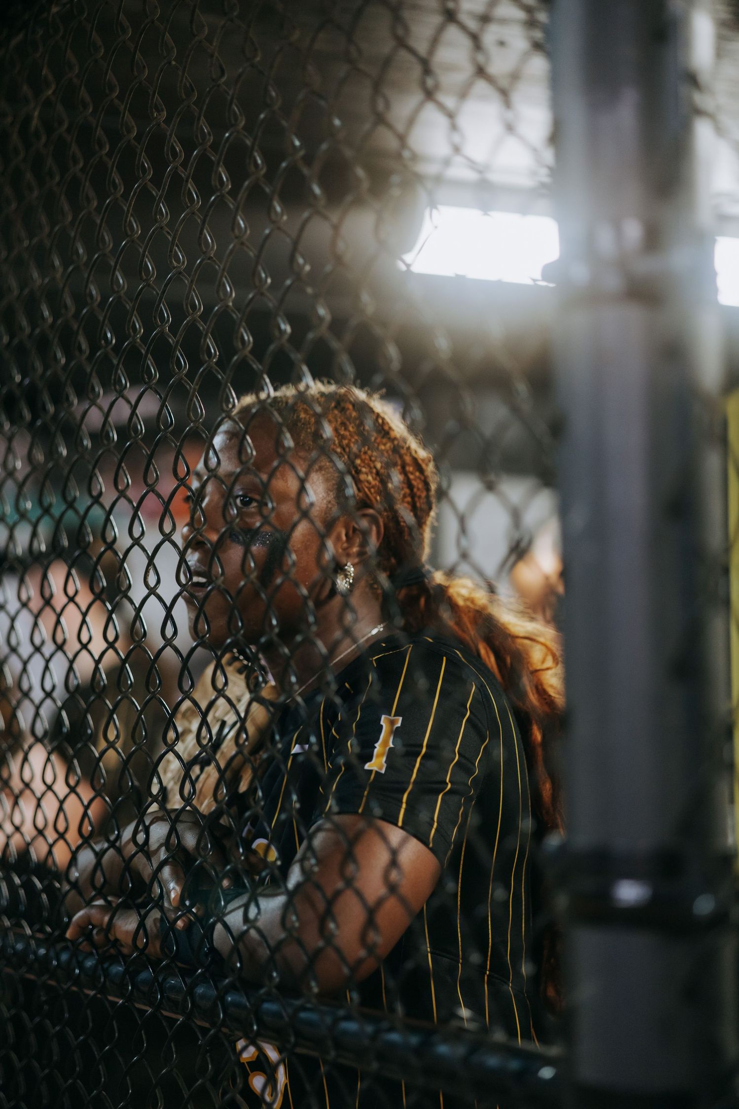 Player in striped uniform seen through chain link fence during night game.