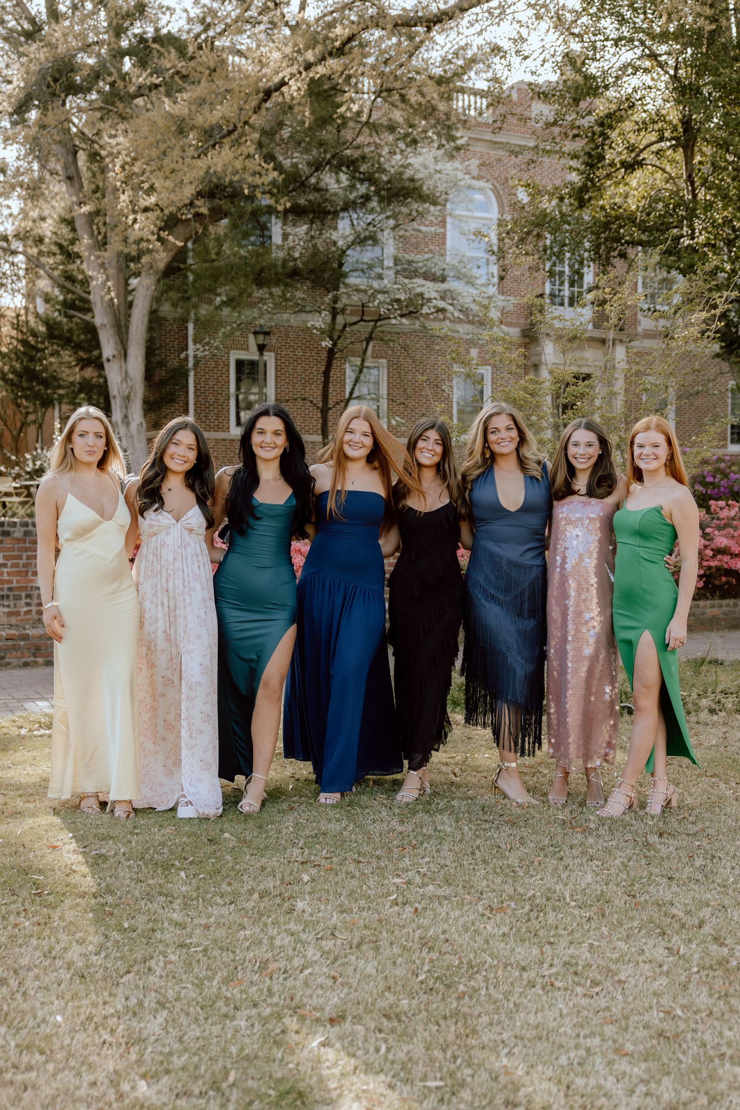 Group of friends in coordinated dresses pose together on campus grounds during spring.