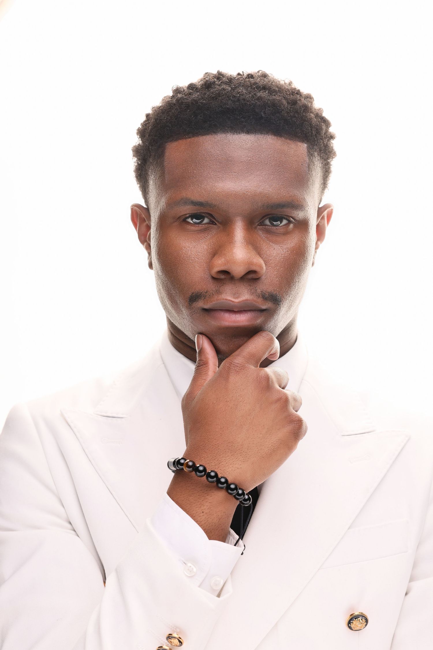 Three stylish portraits of a person wearing a white blazer with gold buttons while posing against a light background.