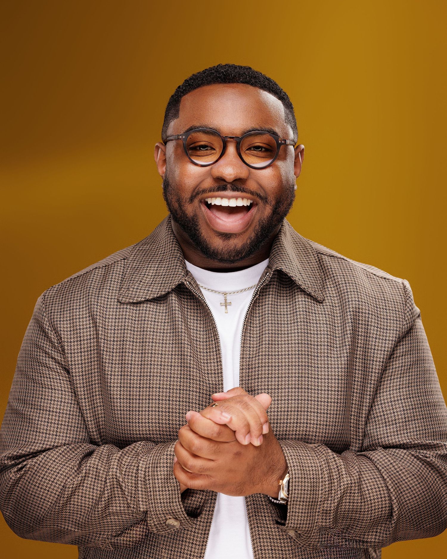 A person wearing glasses and a brown plaid blazer poses against a warm orange background with various expressions.