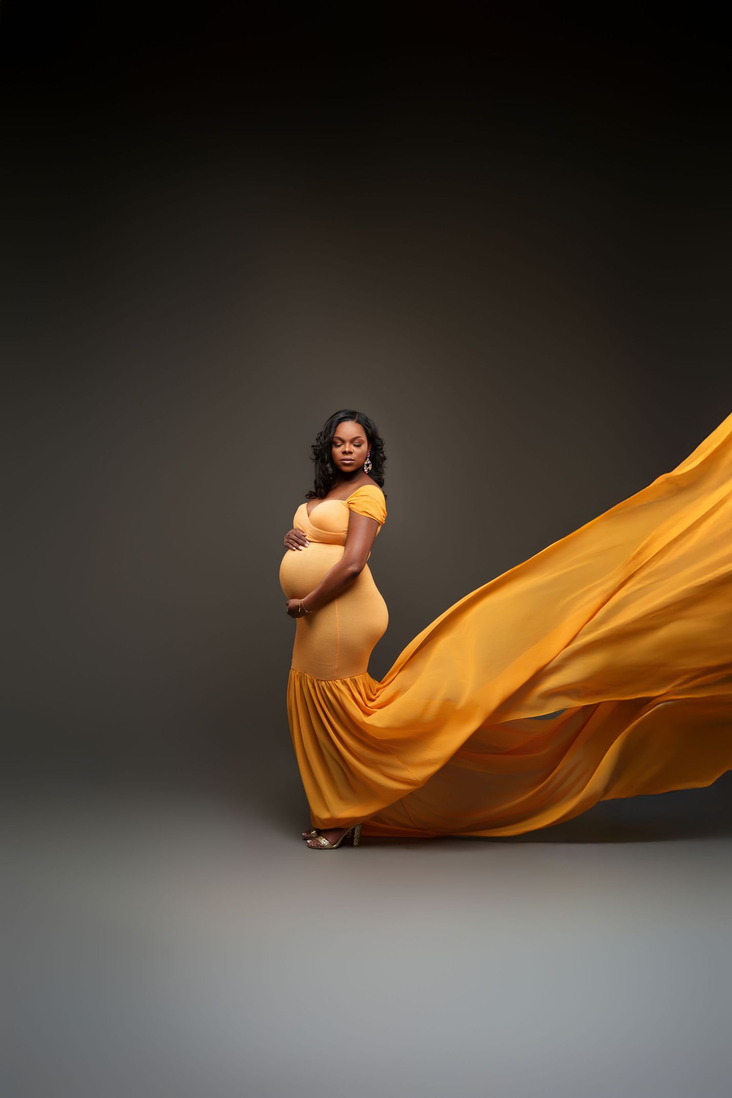 A pregnant mom in a flowing orange dress creates graceful movement against a dark studio backdrop.