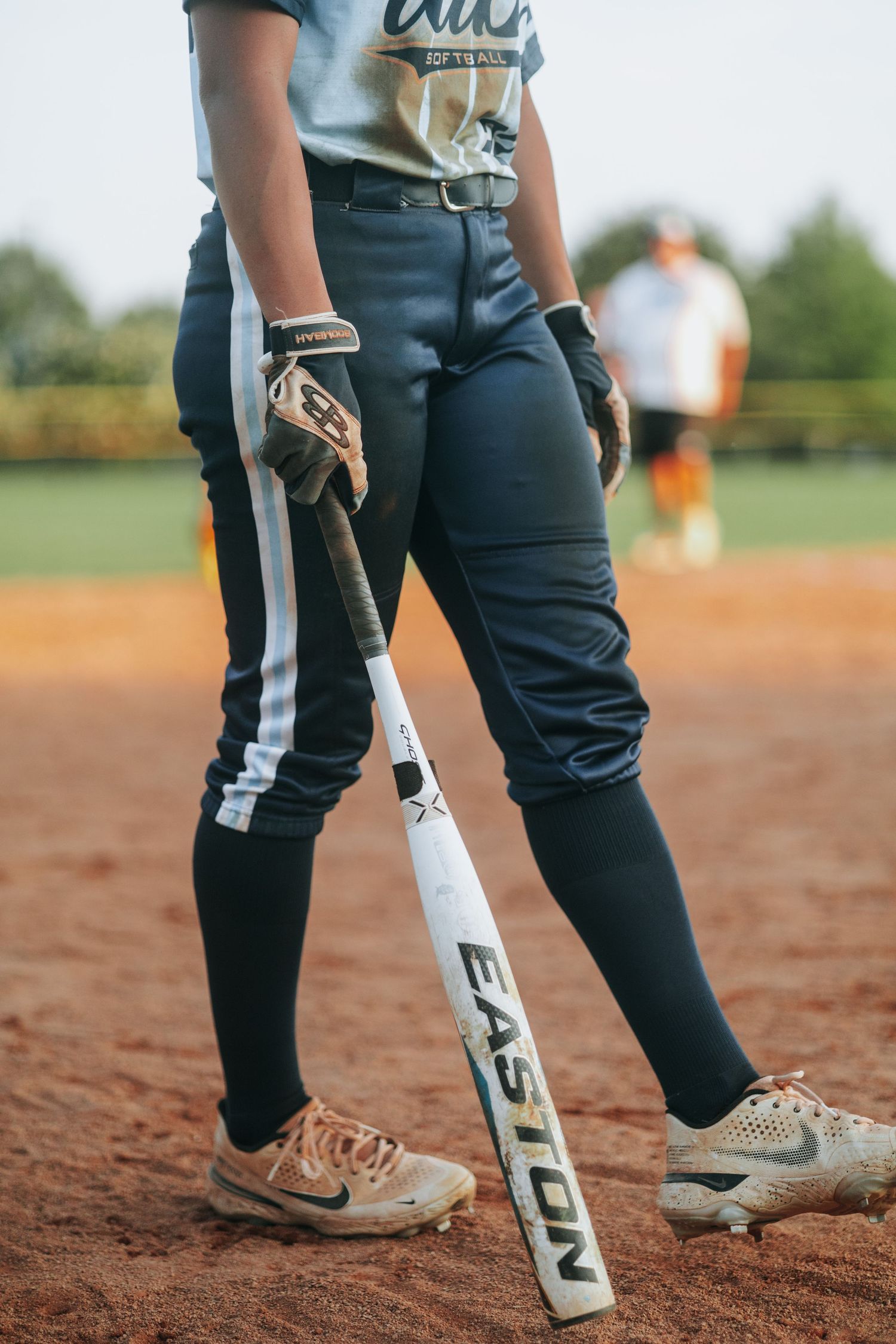 Close-up view of softball players' legs and cleats on the dirt infield.