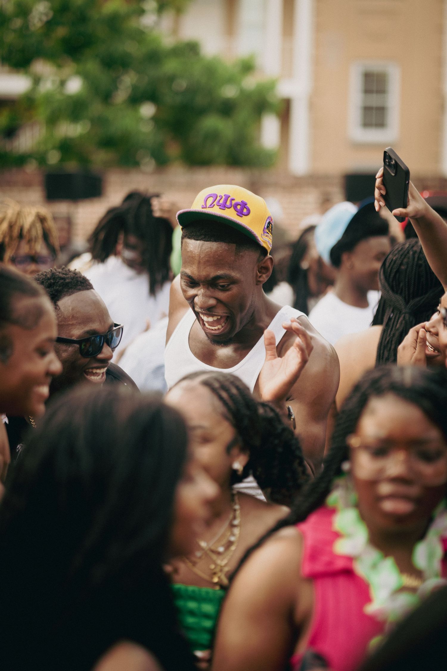 A joyful crowd of people at an outdoor gathering, with one person wearing a Lakers cap in the center.