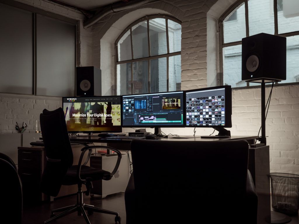 Professional video editing workstation with dual monitors and audio equipment in a modern office space with arched windows.