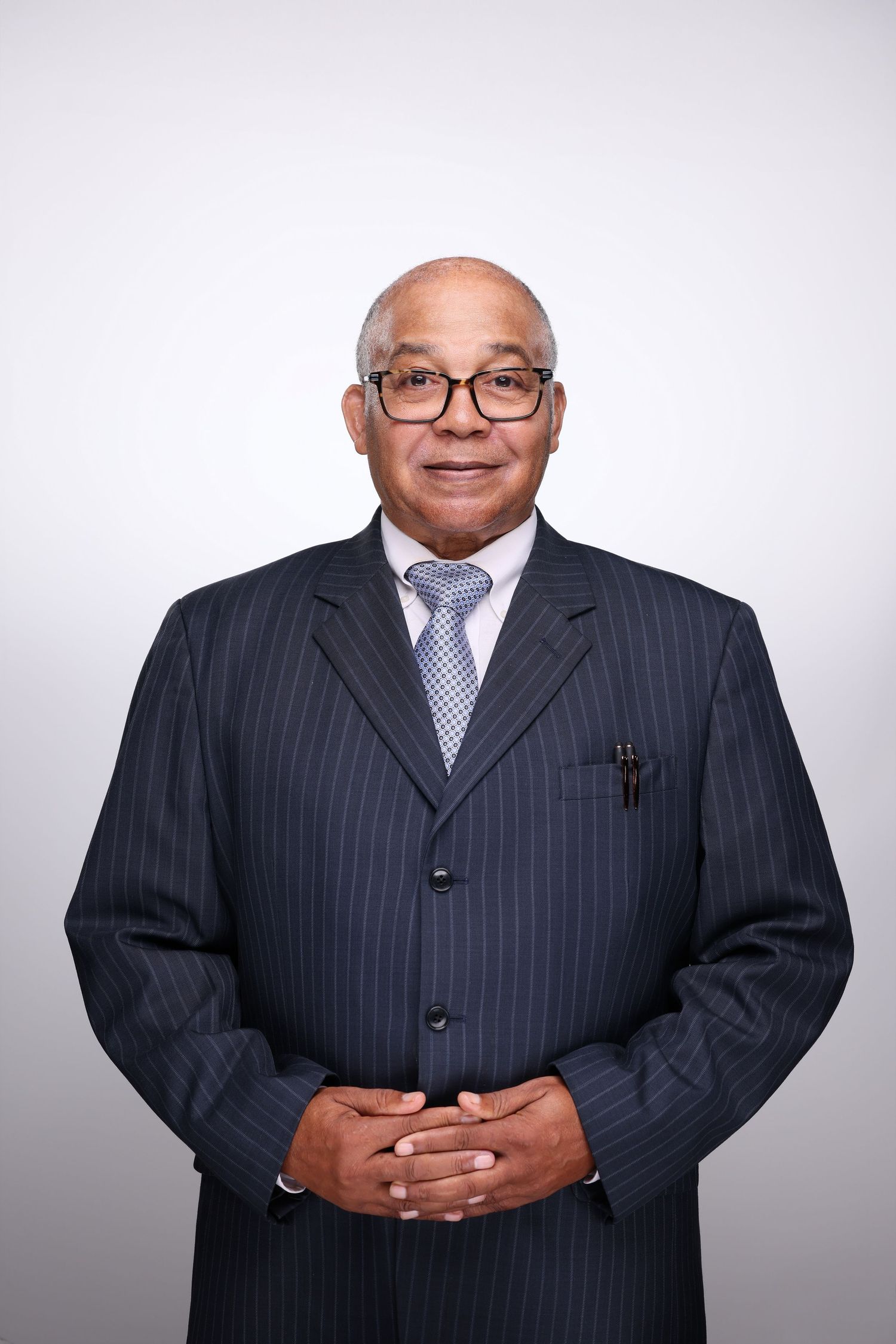Elderly businessman in pinstripe suit and glasses smiling with hands clasped.