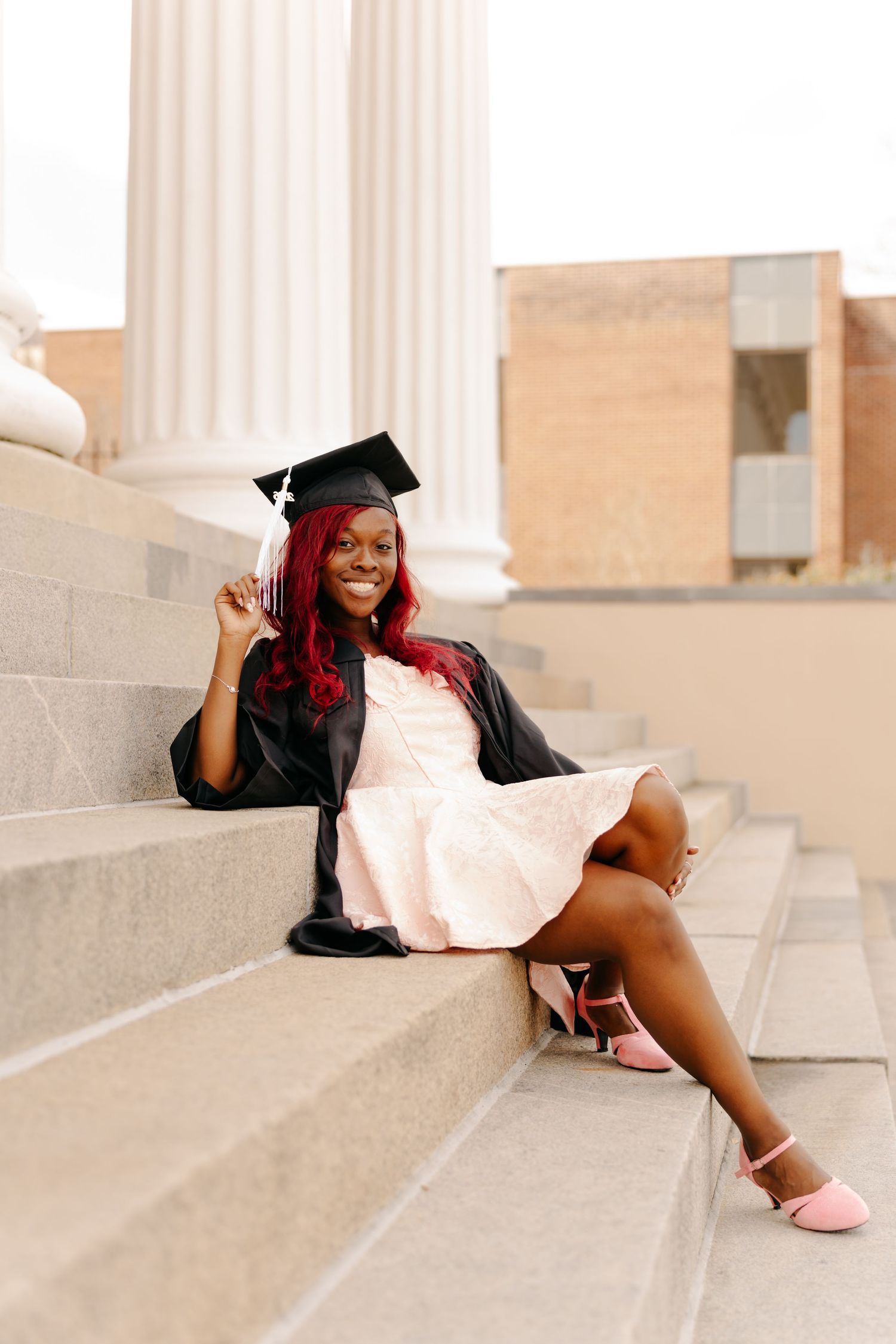 Graduate in cap and gown poses on stone steps while celebrating commencement in a creative photo series at the University of South Carolina.