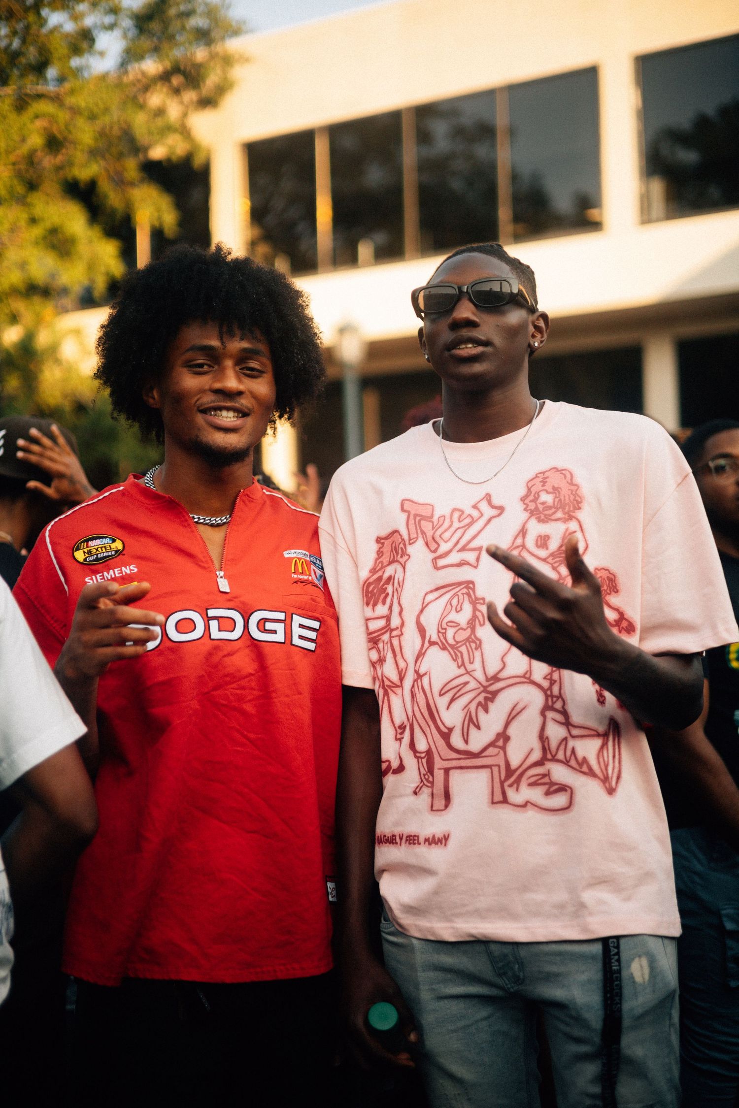 Two people standing together outdoors, one wearing a red Dodge jersey and another in a white graphic t-shirt.USC Hip Hop Wednesday