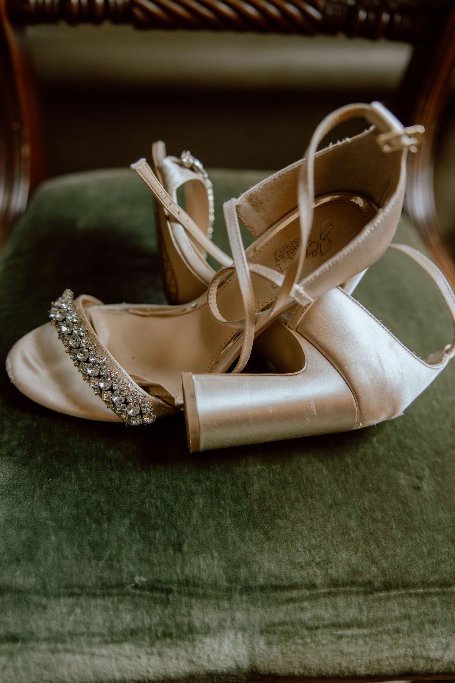 Elegant white bridal shoes with crystal details on green velvet surface.