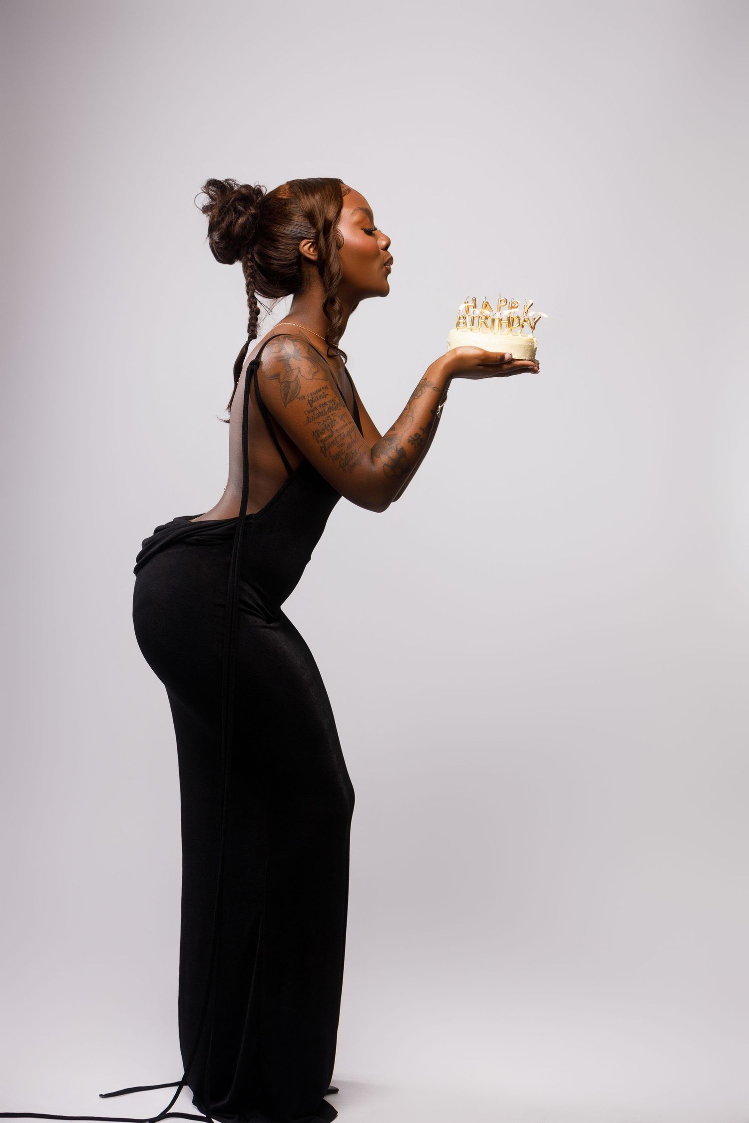 Creative portrait of person in black dress blowing birthday message against white background.