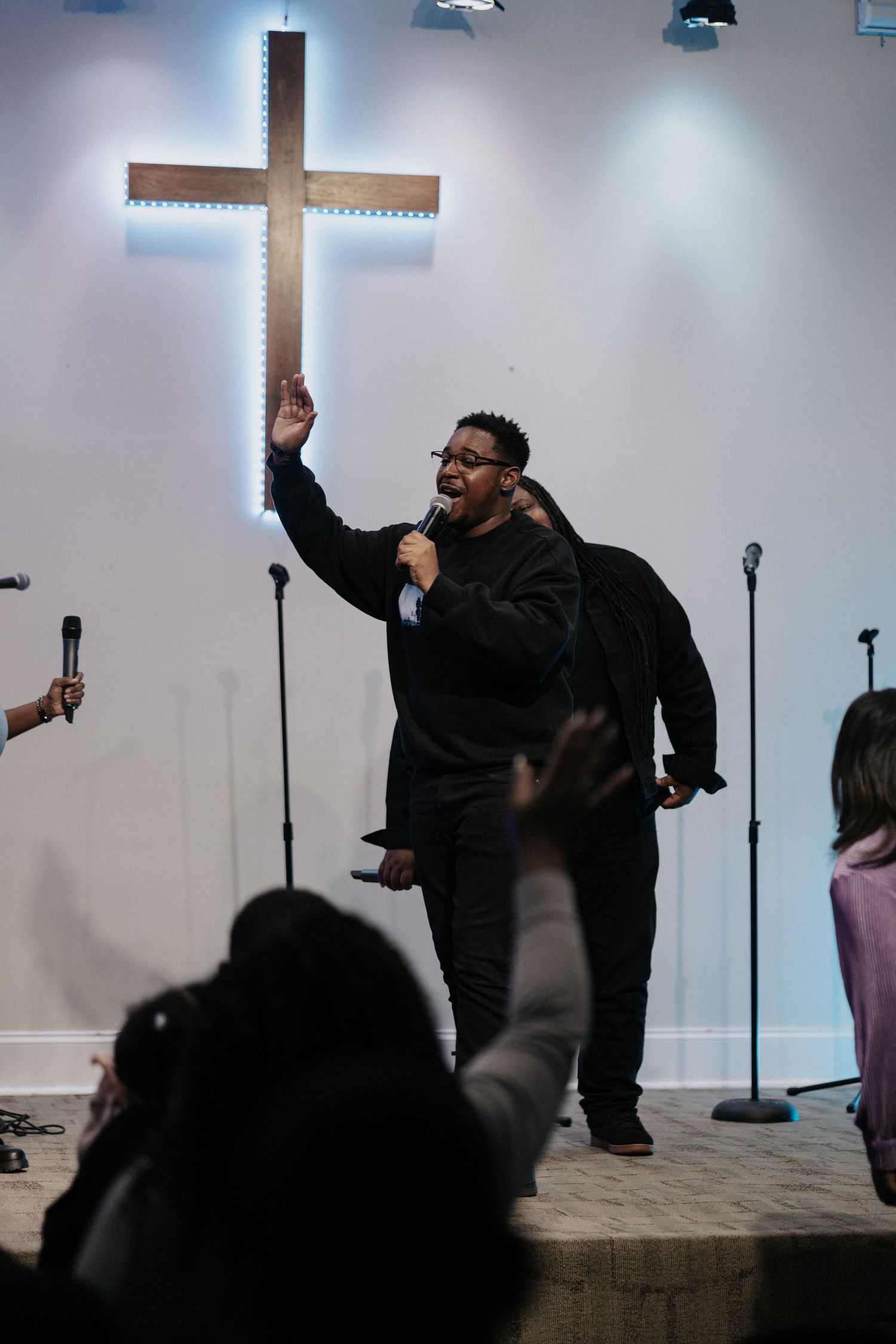 A passionate performance during a church service with a backlit cross and raised hands from the audience.