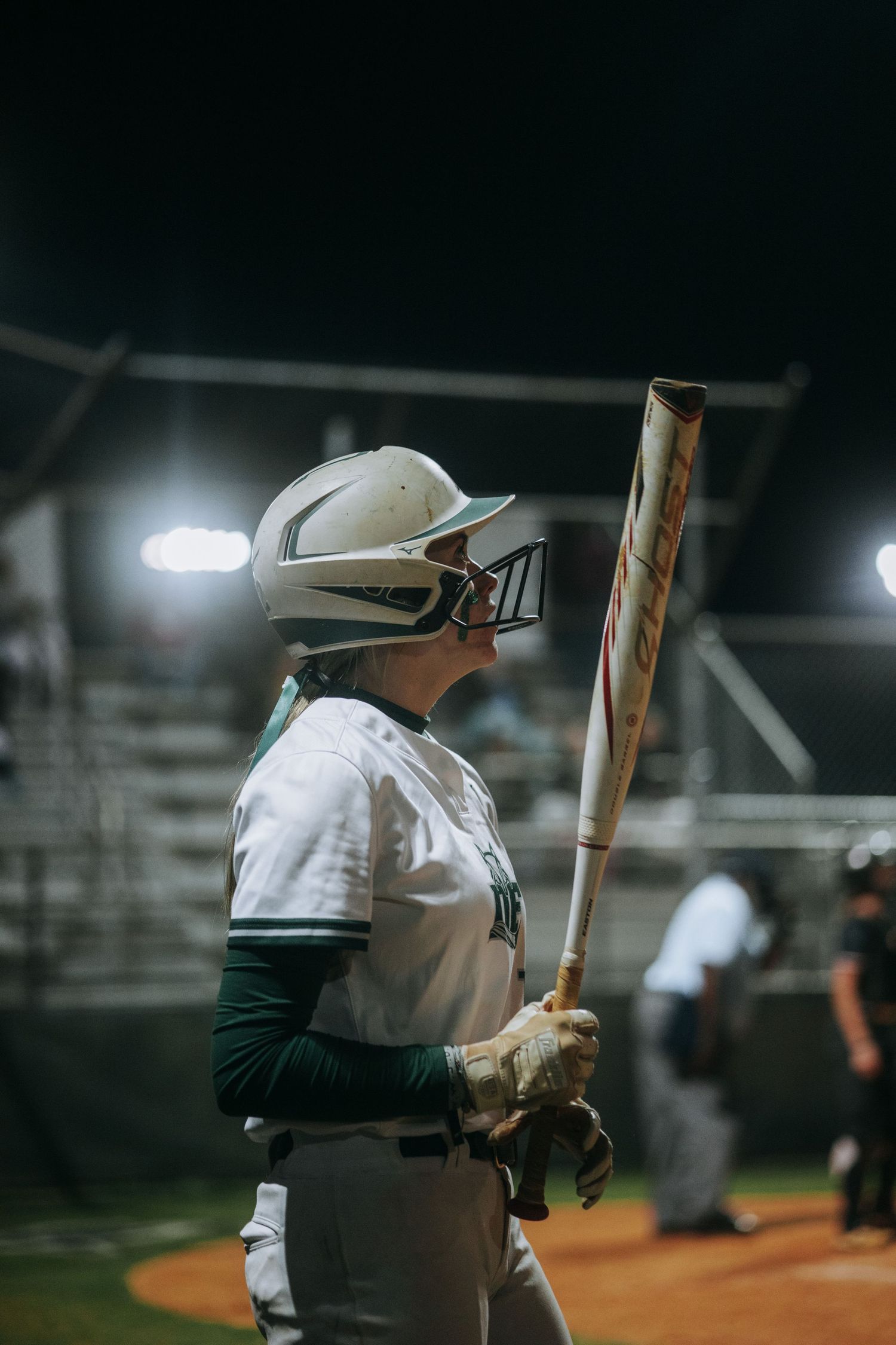 Baseball players in white uniforms practicing batting at night under stadium lights.