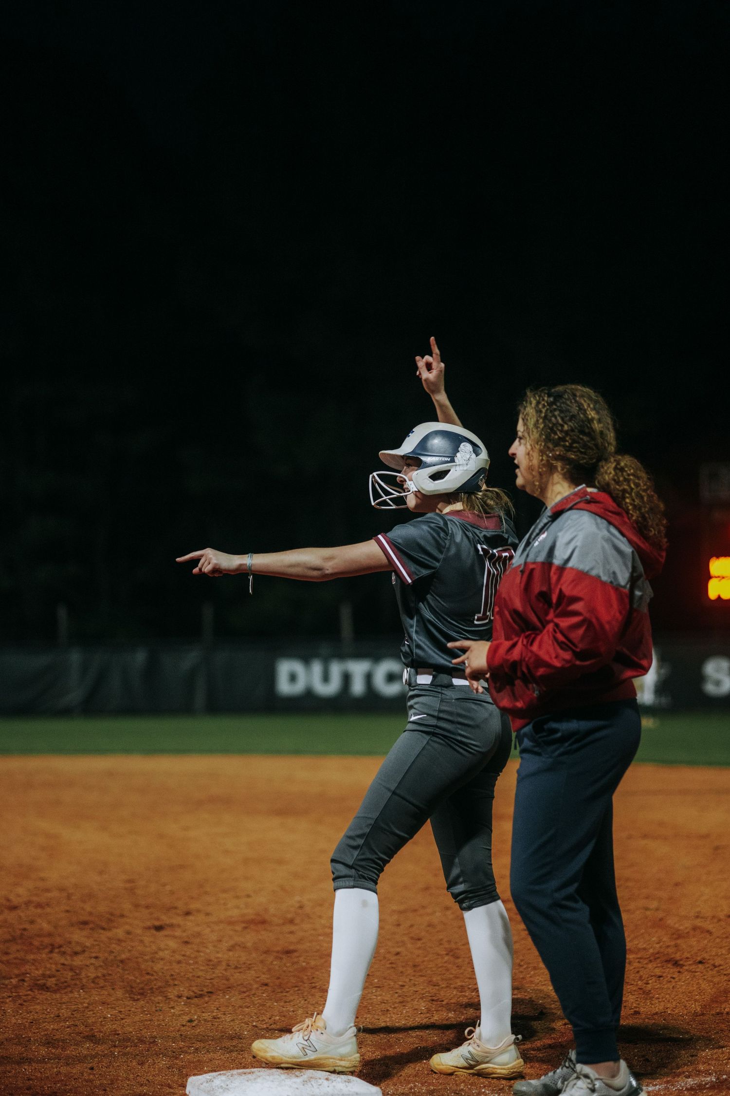 Softball player and coach interact on the field during a night game.