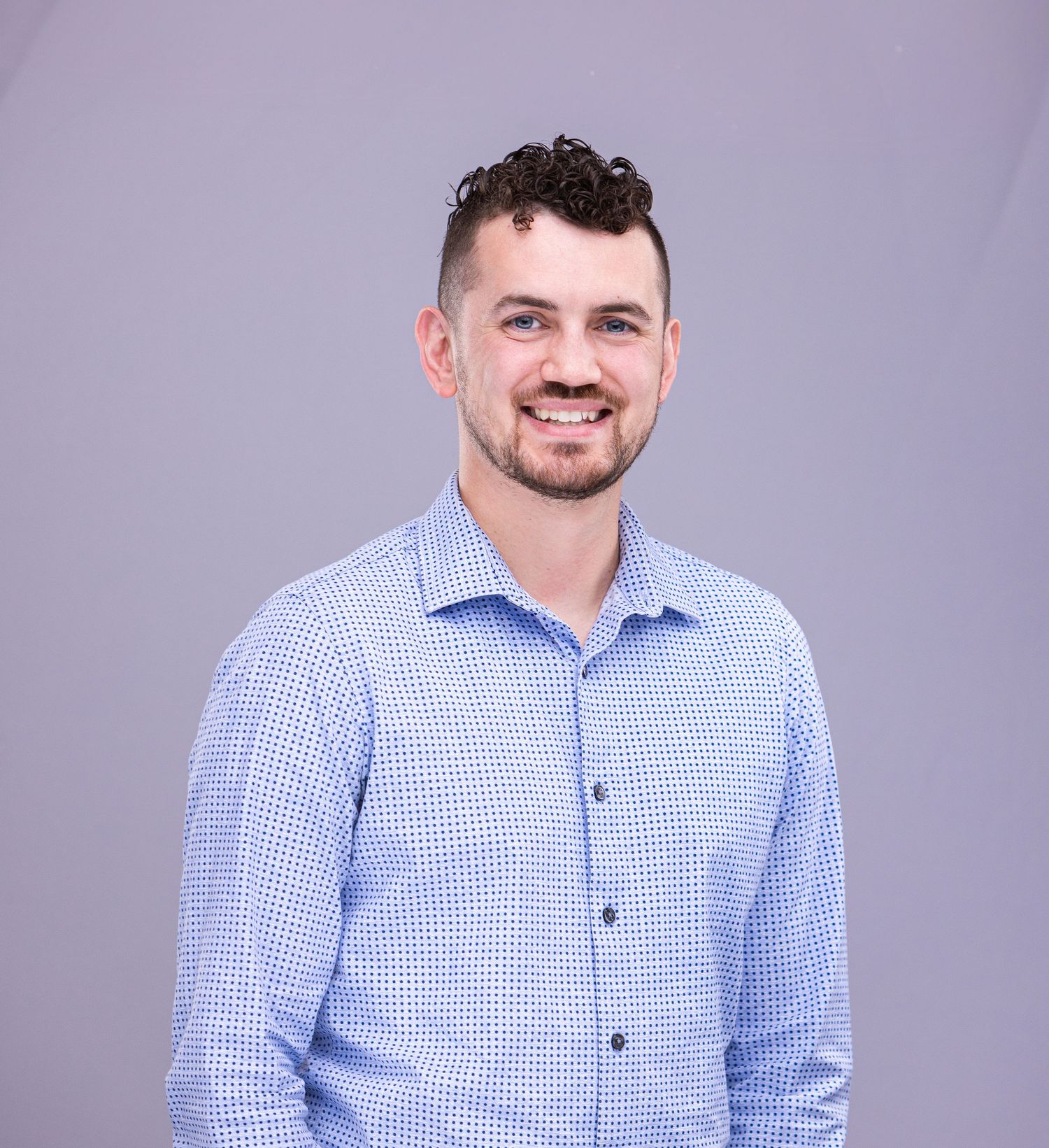 Professional headshot of person in blue gingham button-down shirt against purple background.