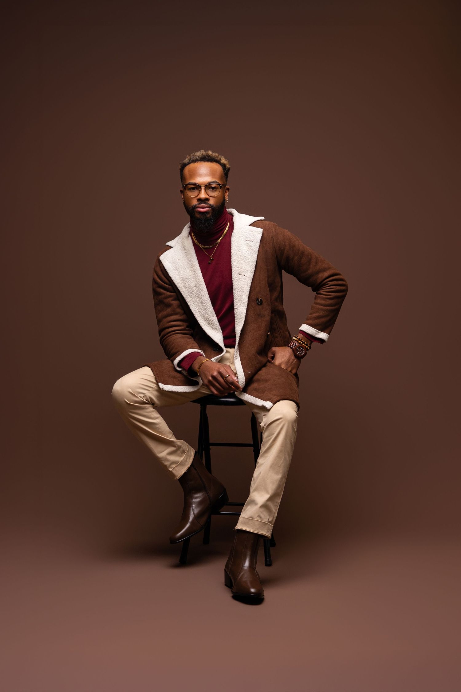 Fashion portrait featuring brown shearling coat and burgundy sweater against brown background.