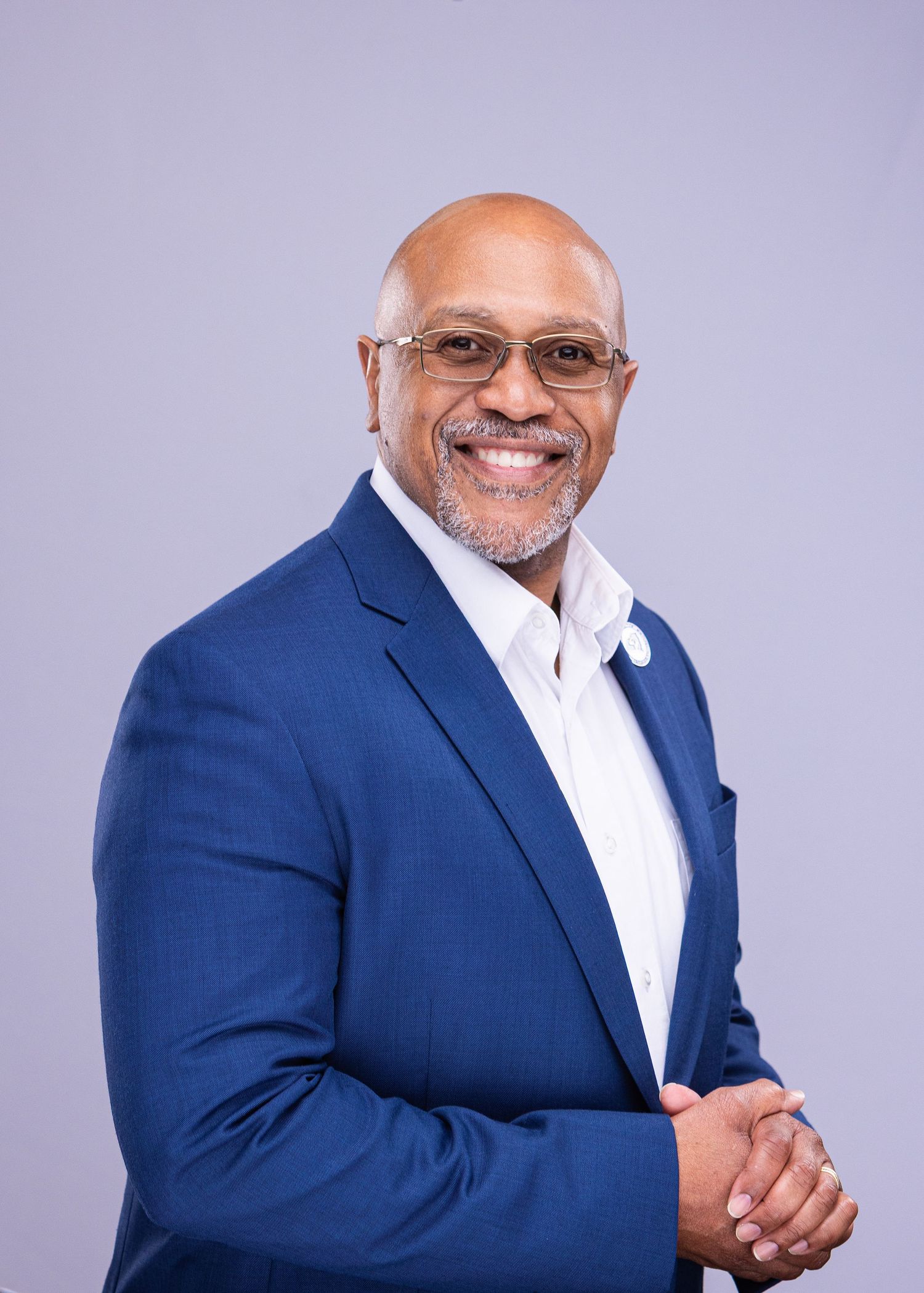 Professional portrait of smiling person in navy blazer and white shirt against purple background.