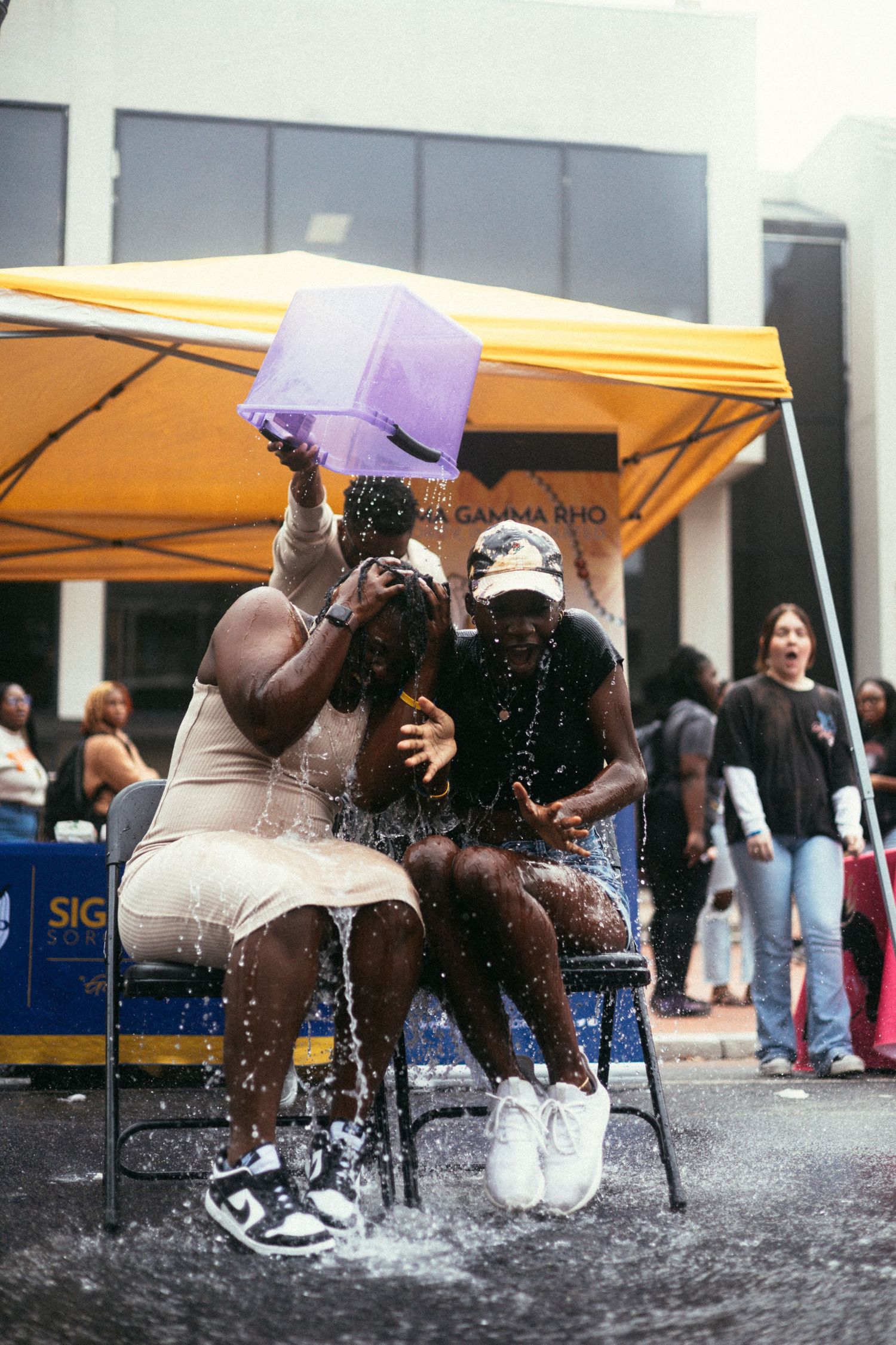 People sit under a yellow canopy tent getting splashed with water during a summer event on a hot day. USC Hip Hop Wednesday