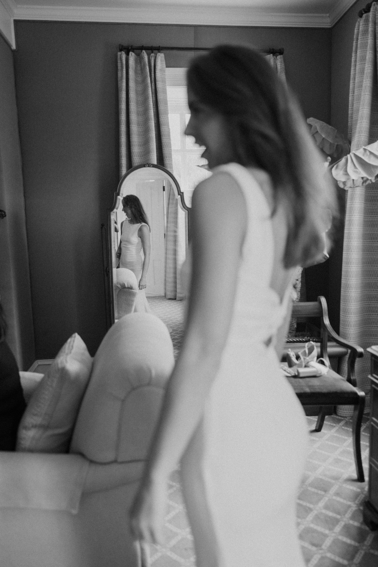 A motion-blurred black and white photo of a figure in a white dress looking at their reflection in a mirror.