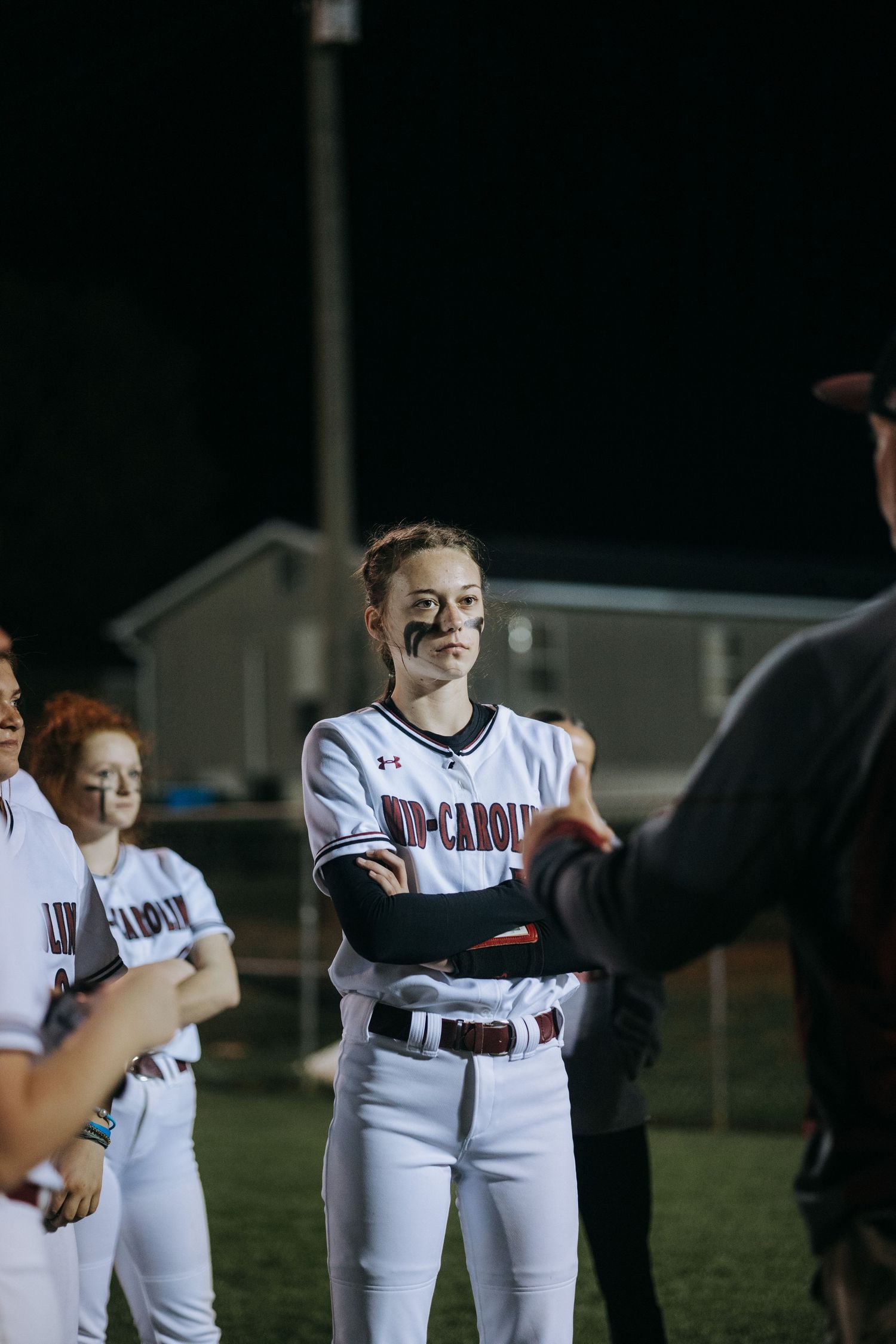 Softball player in white uniform smiling during nighttime game.