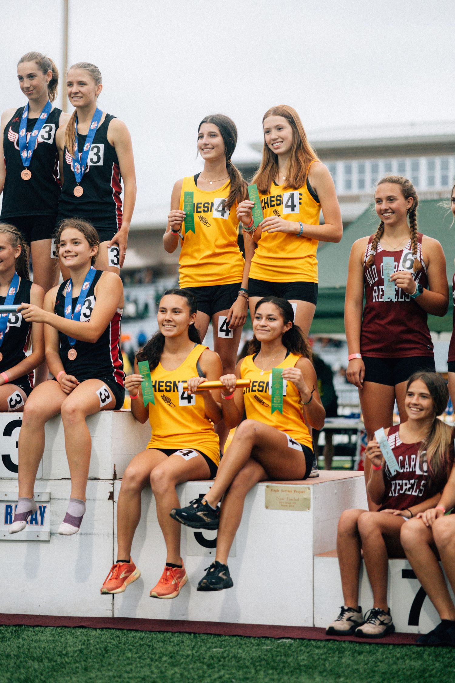 Athletes in yellow and dark uniforms sitting on bleacher steps at track meet.
