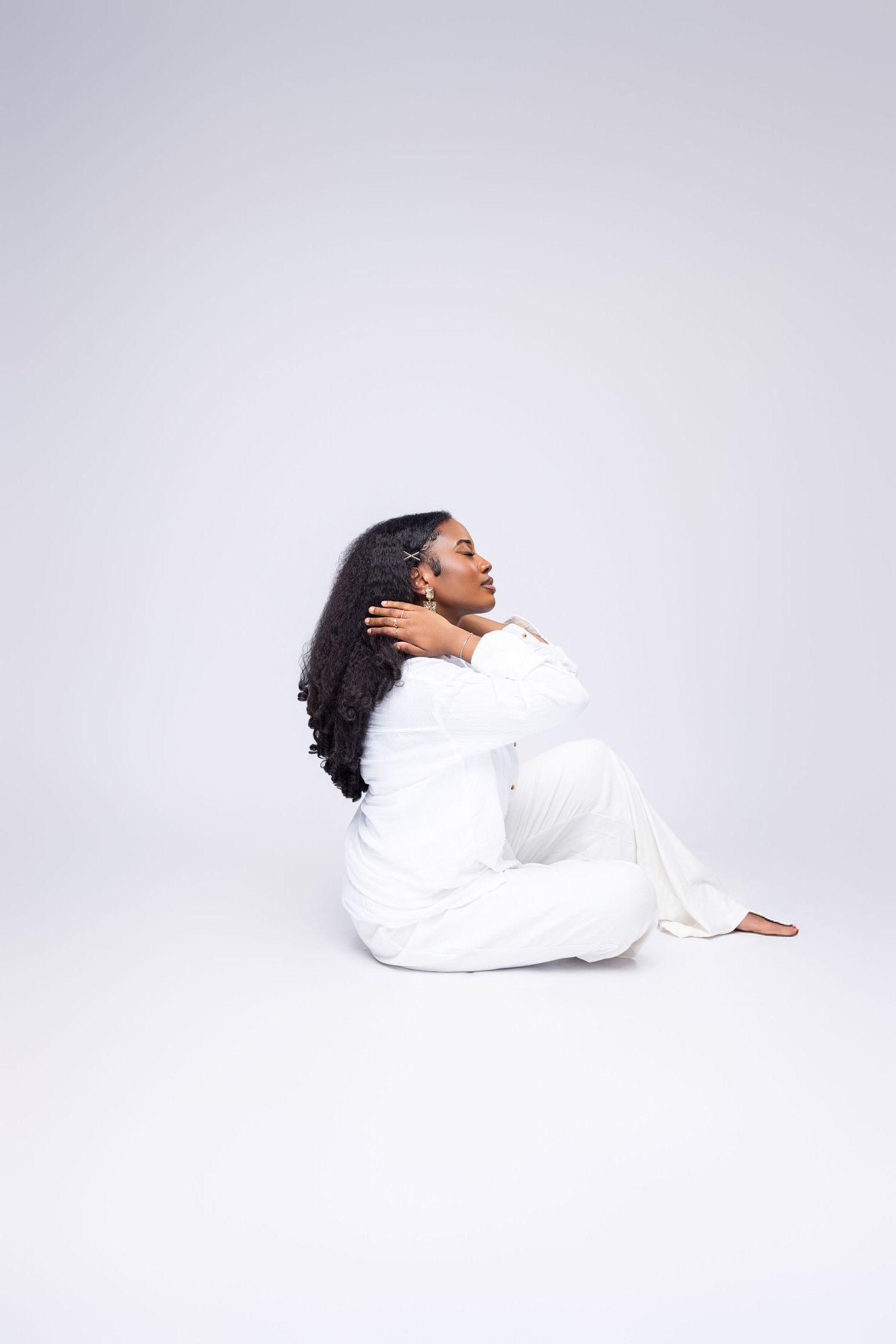 Figure in white attire reclining on light background in minimalist photo series.