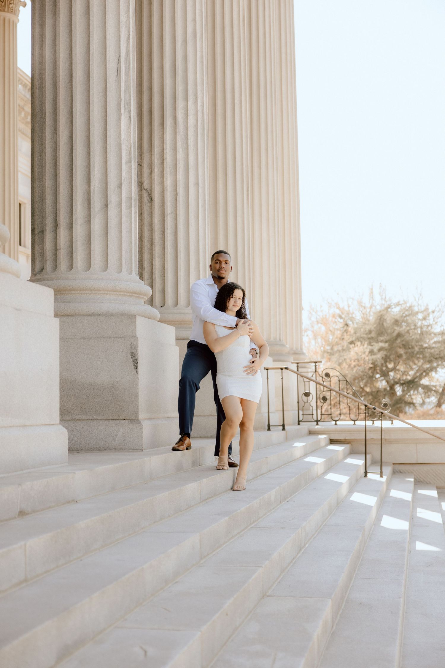 Romantic couple embraces on marble steps between classical columns.