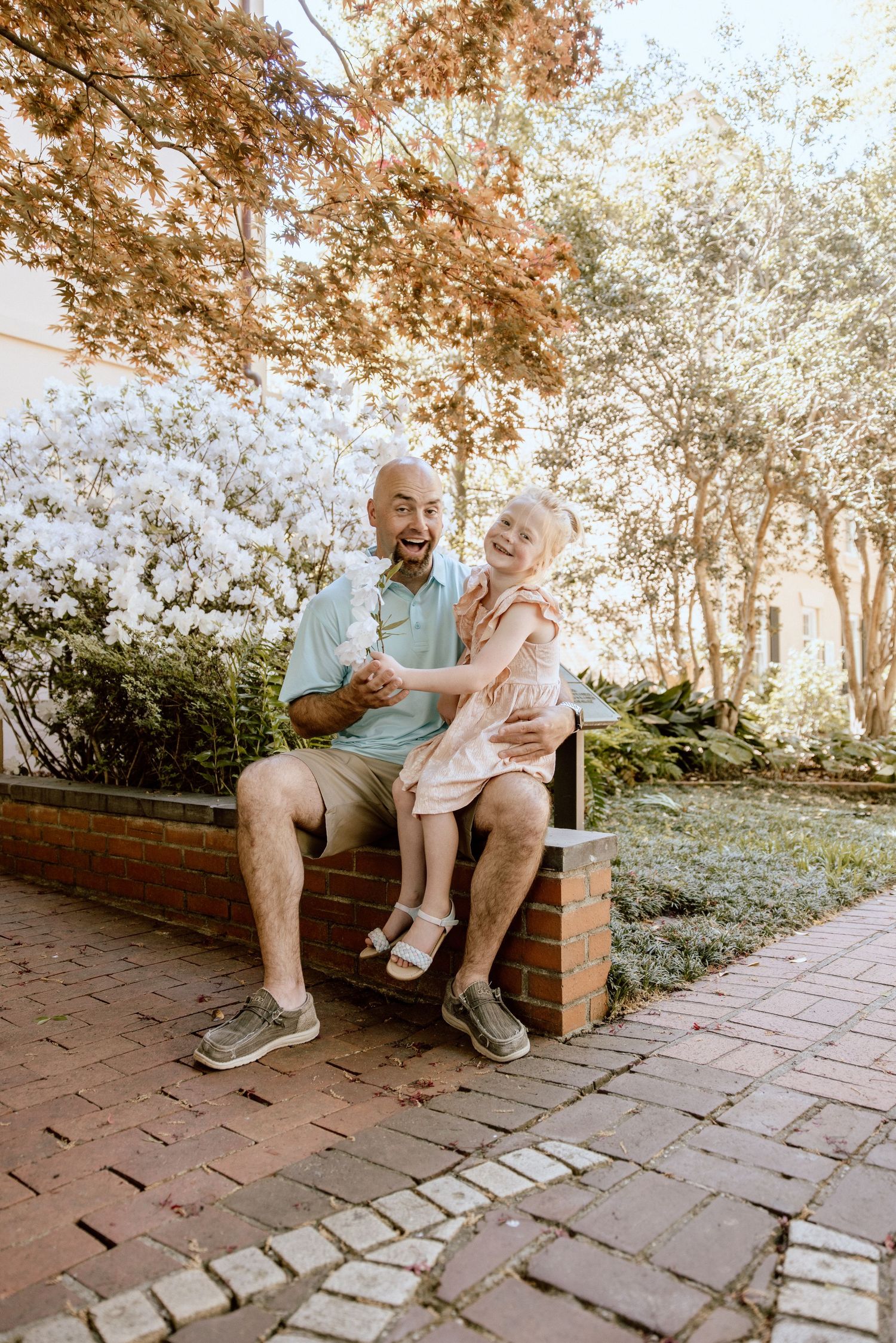Parent and child sharing joyful moment while sitting on brick wall outdoors.