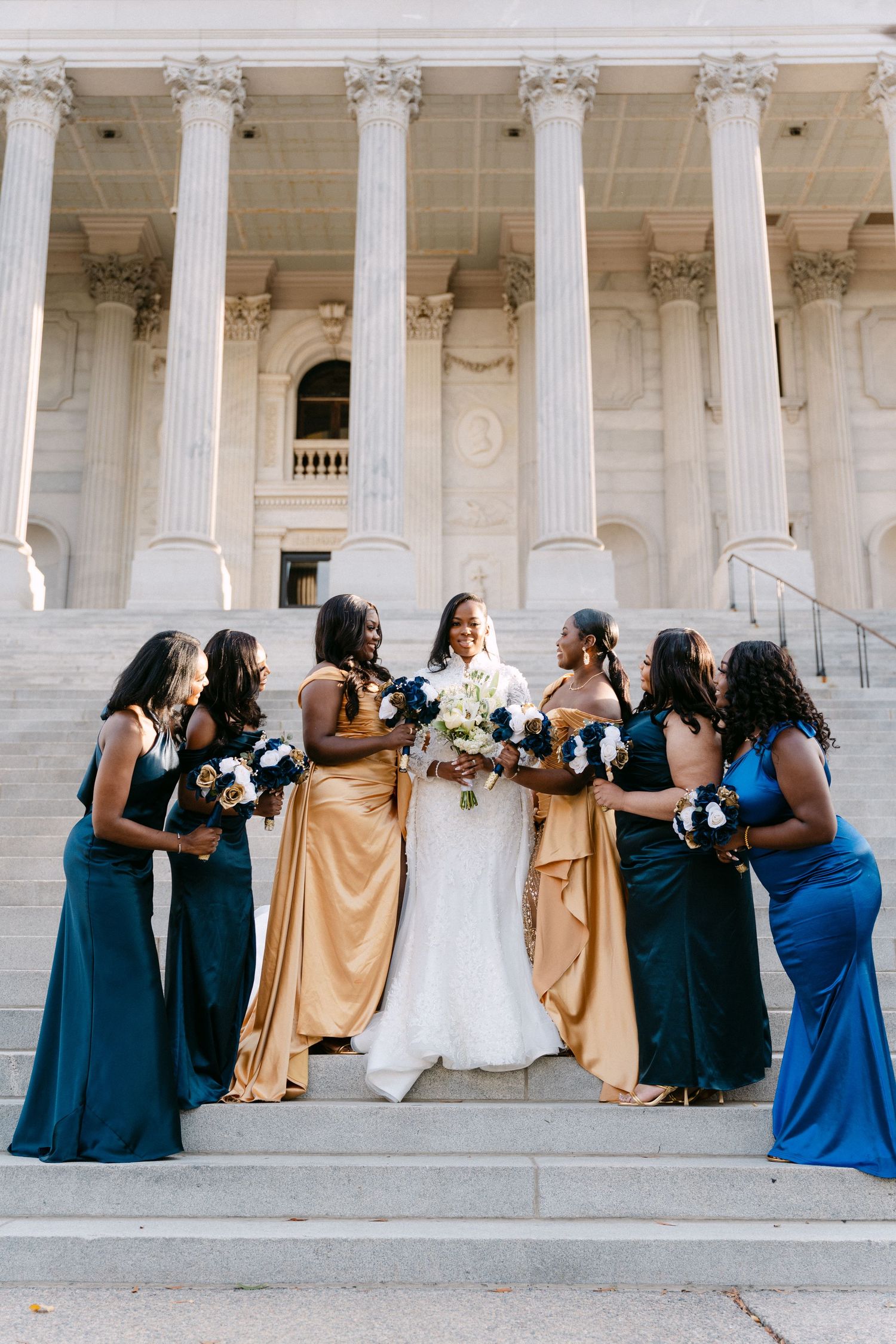 Wedding party in navy blue and gold dresses poses against white columned building in creative sequence photos.