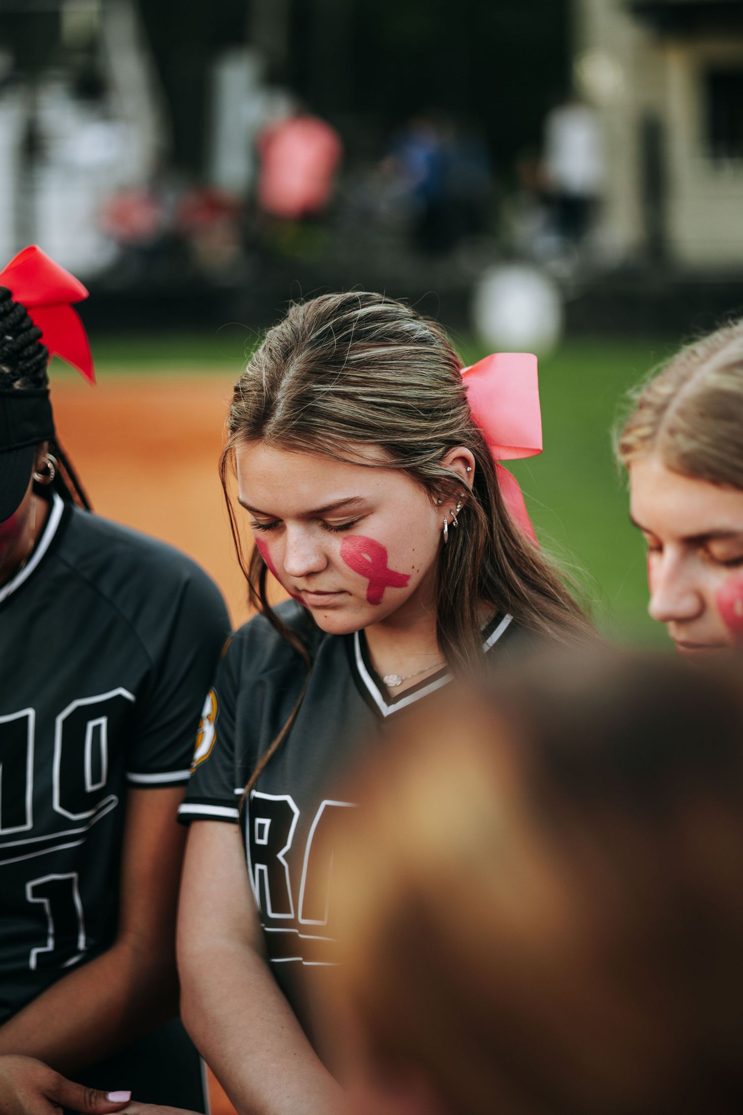 Irmo HS Softball players in black uniforms with pink bows gathering for team meeting.