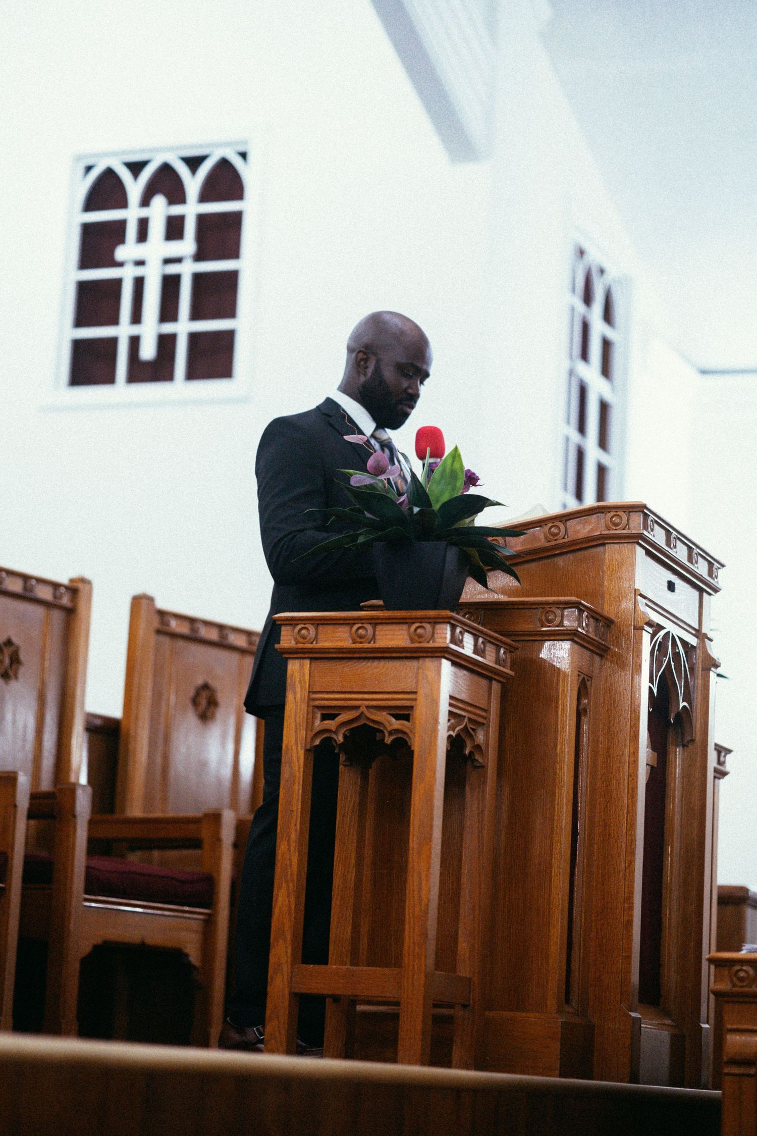 A speaker stands at an ornate wooden pulpit in a traditional church setting with gothic windows.