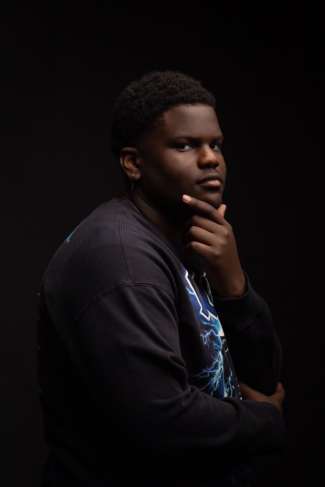 Portrait of person in dark clothing against black background with thoughtful expression.