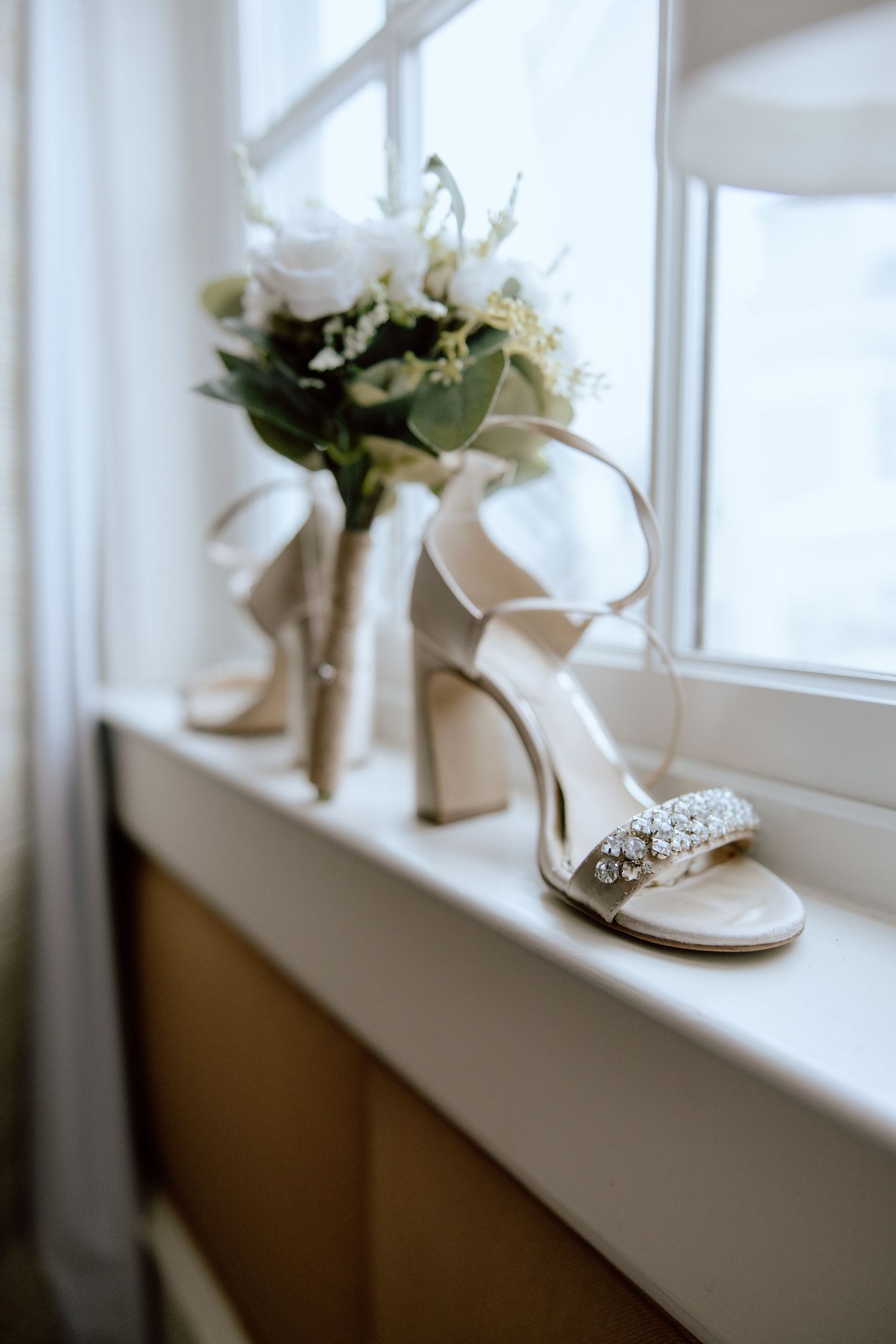 Elegant bridal shoes and white rose bouquet on windowsill in natural light.