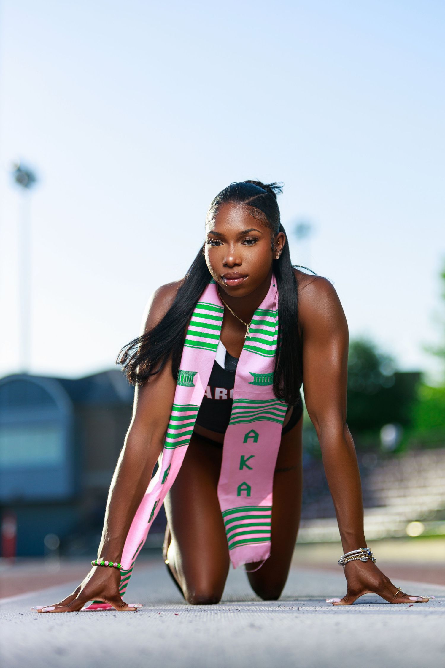 An athlete in starting position wearing a pink and green stole on an outdoor track.
